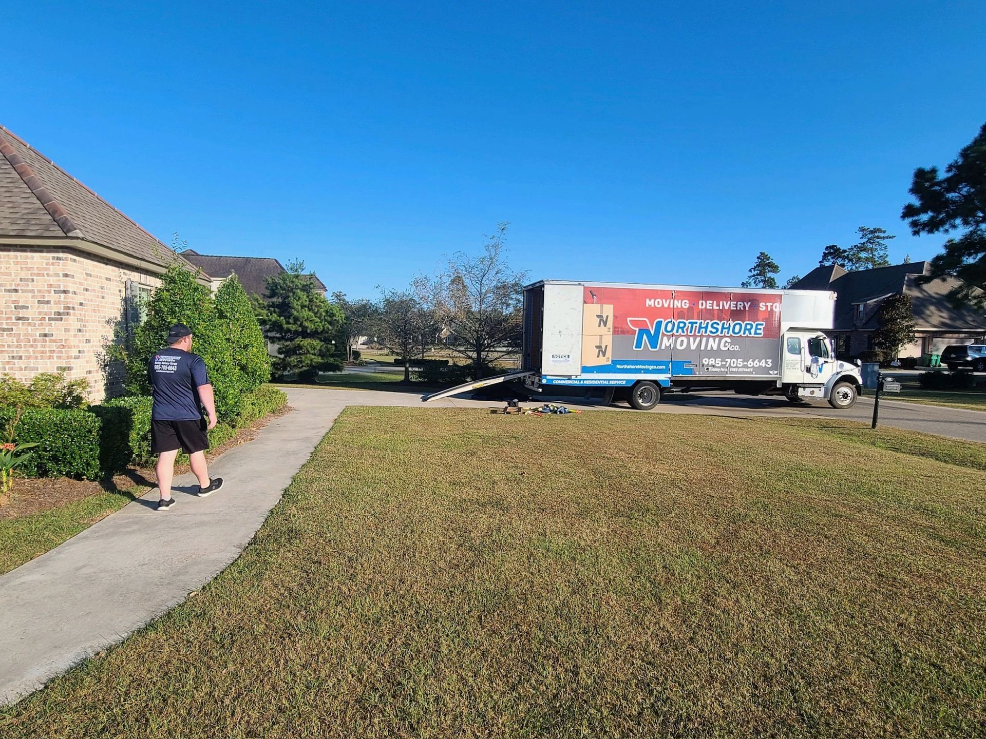 A person in a blue shirt walks on a sidewalk next to a house, with a parked NorthStar Moving truck visible on the street.