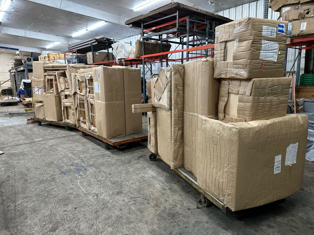 Warehouse aisle with stacked cardboard boxes and wrapped pallets on metal shelving and carts