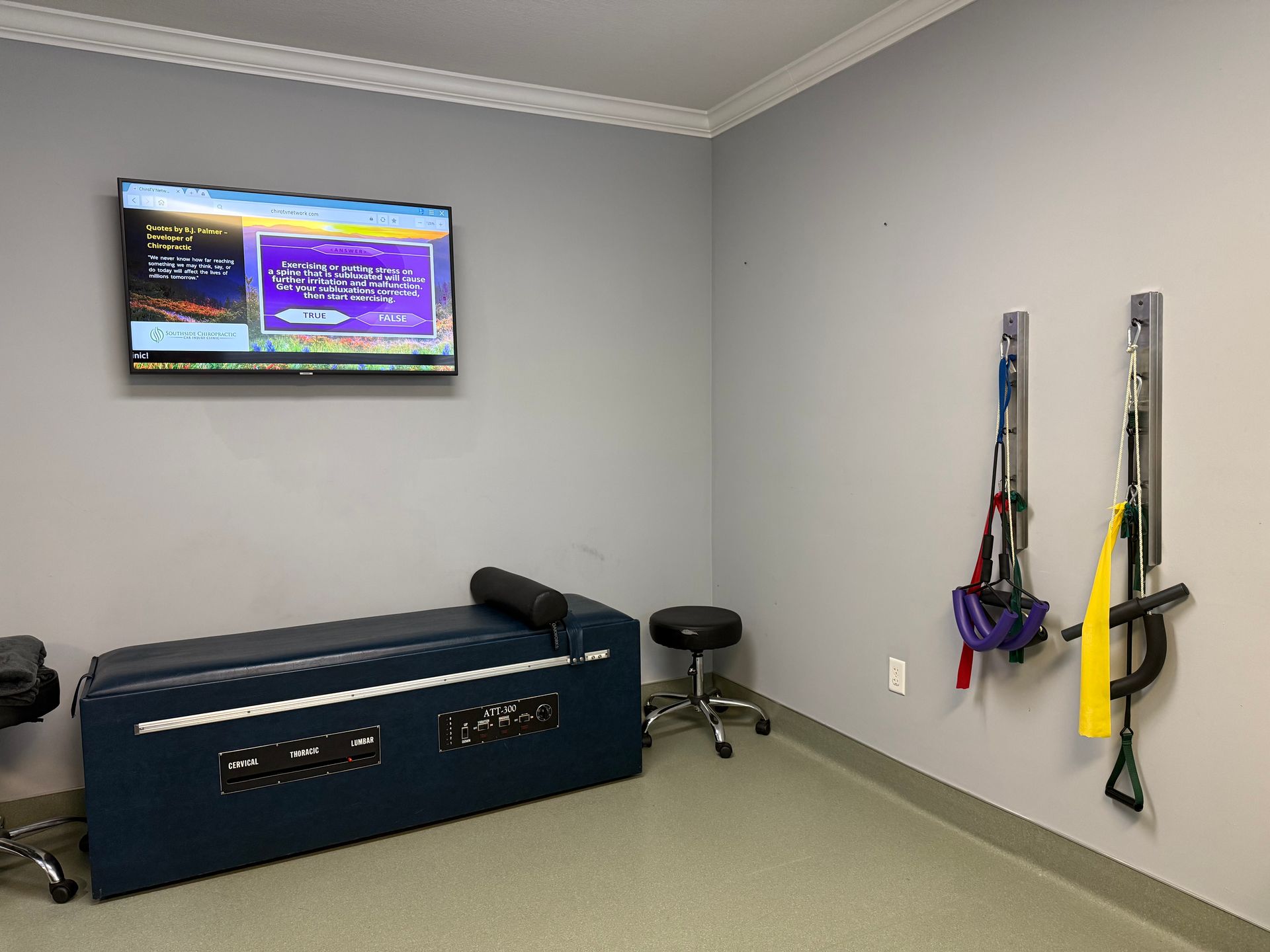 Clinic room with exam table, TV, and resistance bands on the wall