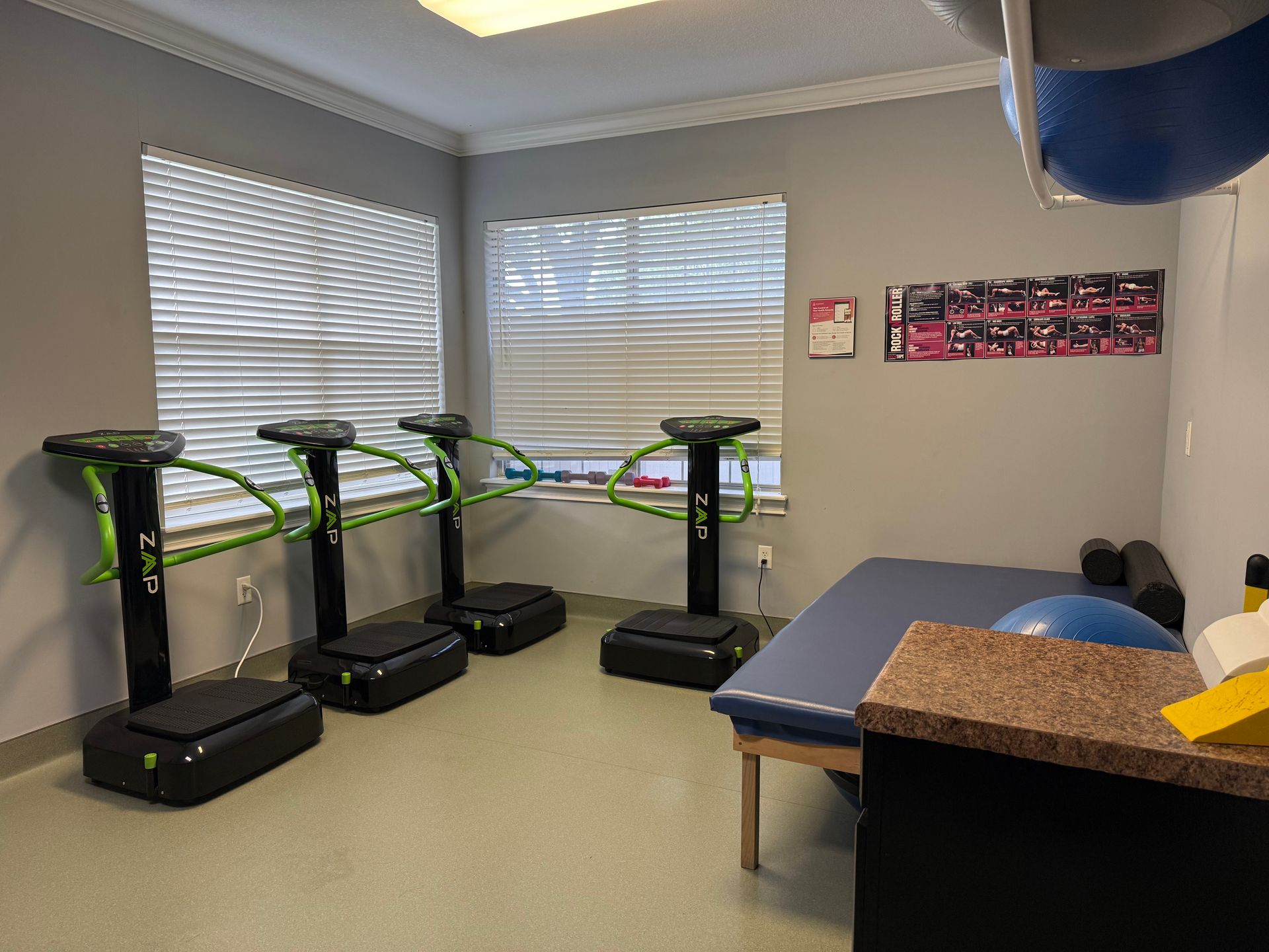 Exercise room with four treadmills, a treatment table, and blinds over two windows.