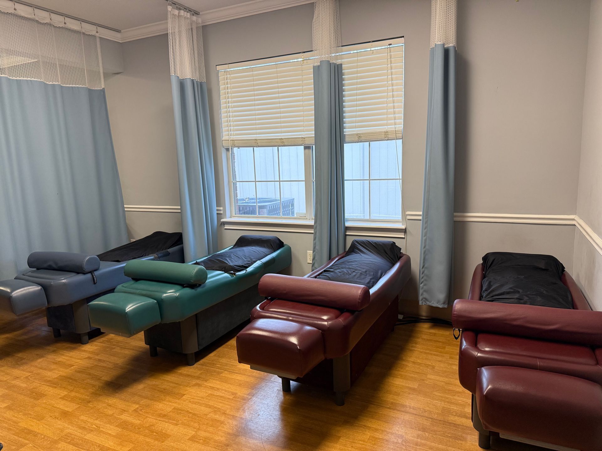 Set of adjustable massage tables in a bright room with large windows and blue privacy curtains
