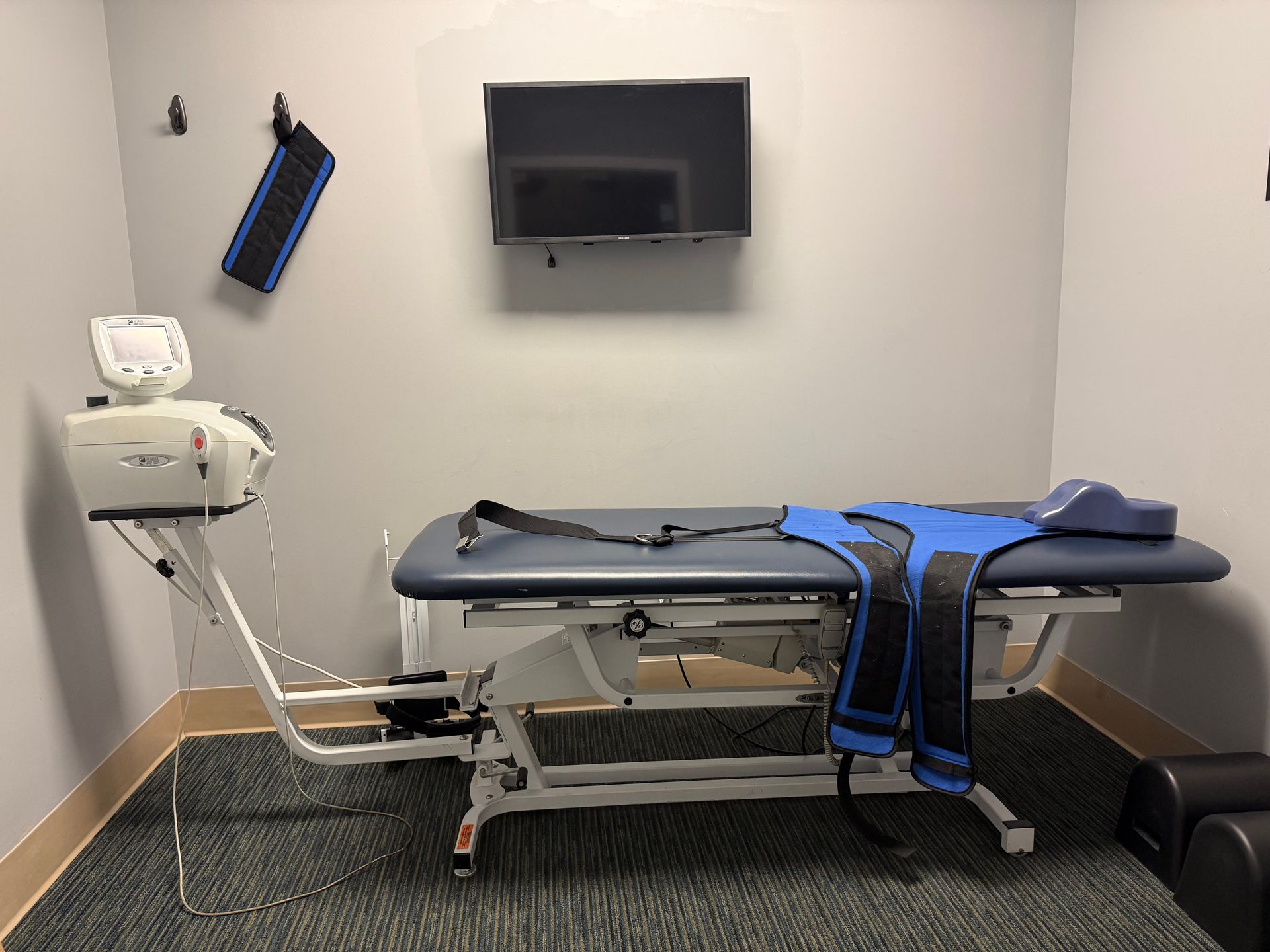 Medical exam room with an examination table, wall-mounted monitor, and patient lifting equipment