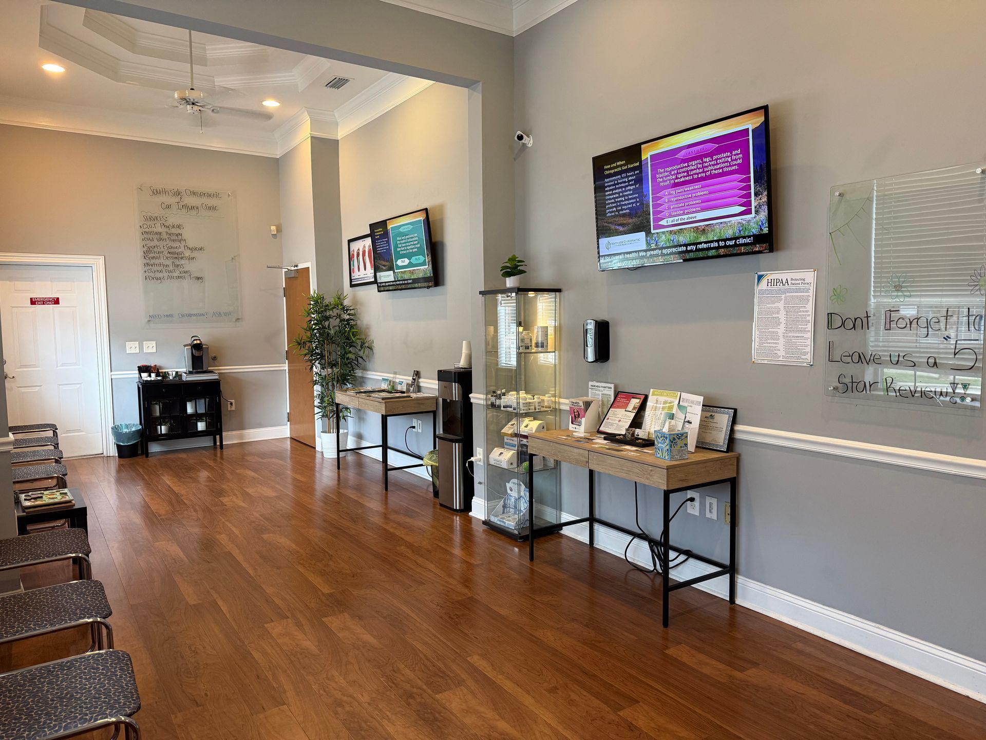 Bright waiting room with wooden floors, wall-mounted TVs, chairs, and a reception table.