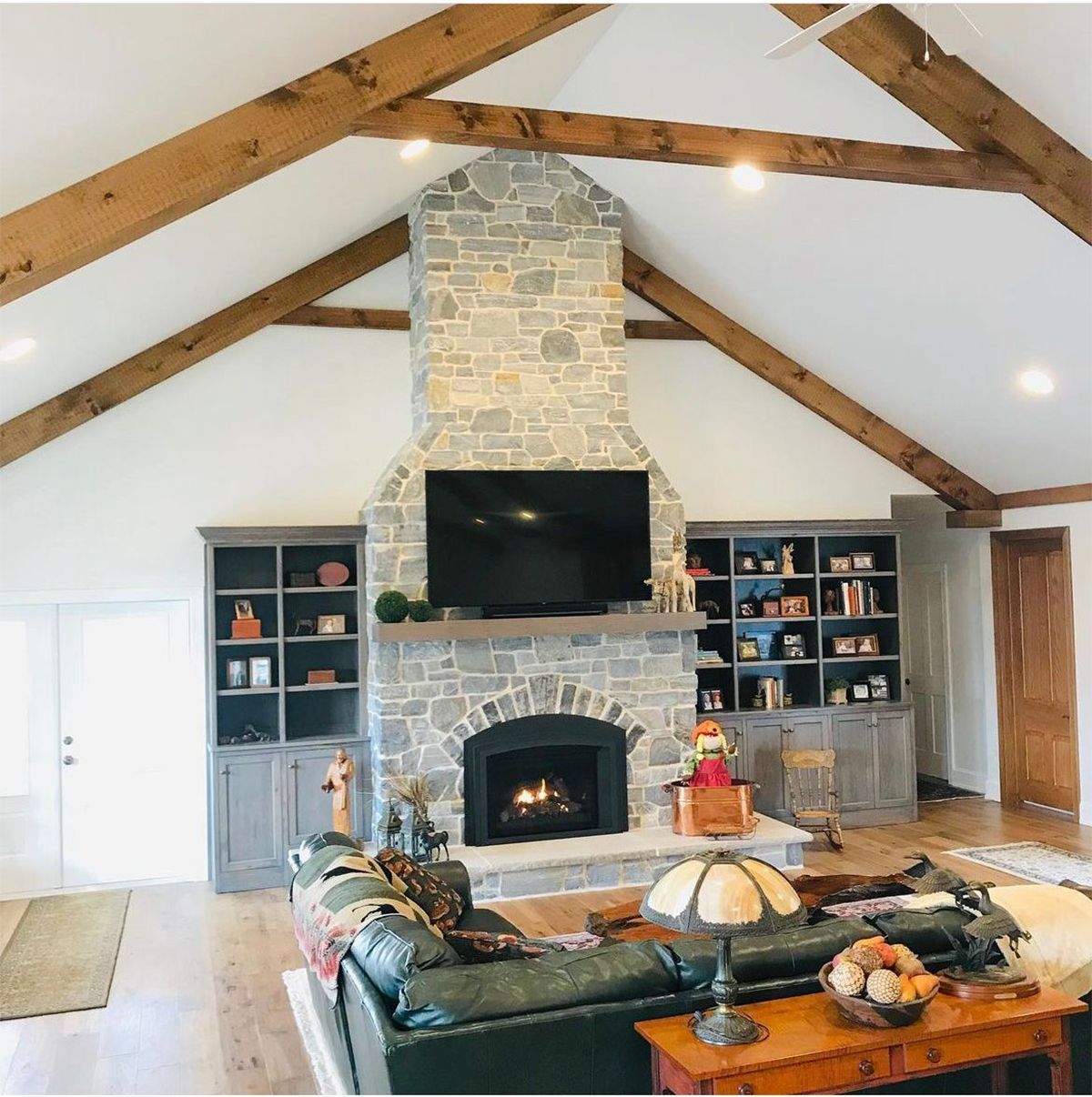 Cozy living room with stone fireplace, mounted TV, exposed wood beams, and built-in bookshelves