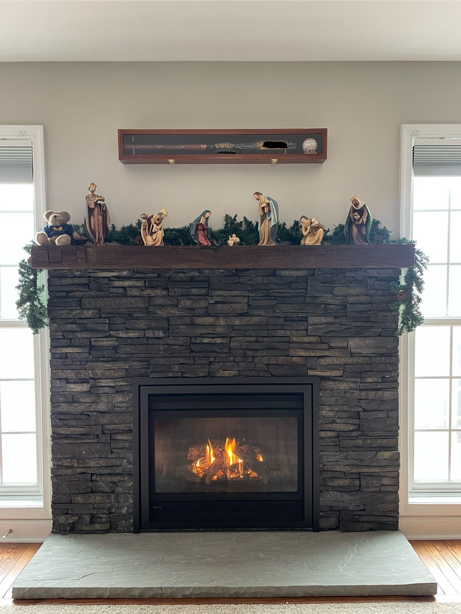 Stone fireplace with a lit fire, decorative mantel, and windows on both sides