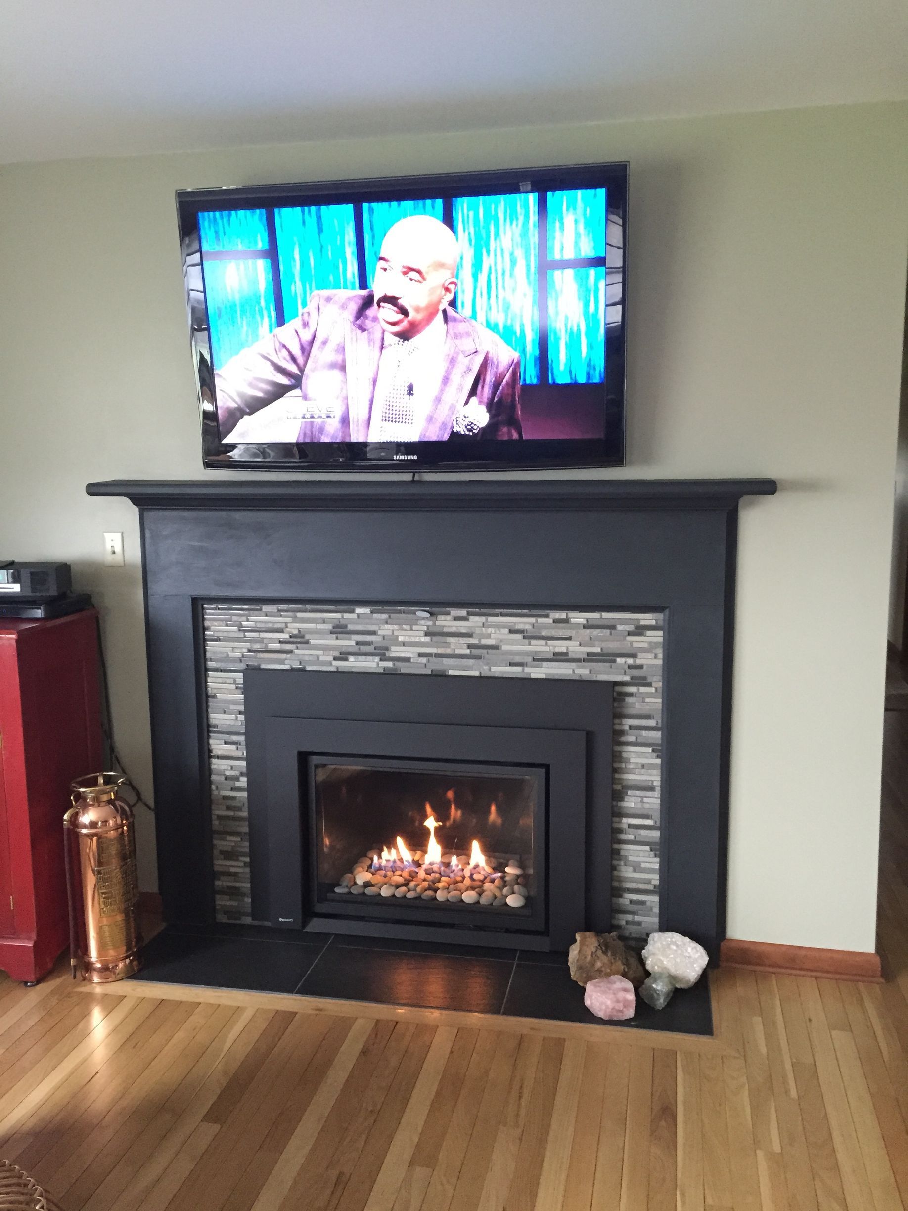 Living room with a TV above a fireplace, wood floor, and decorative fireplace tools.