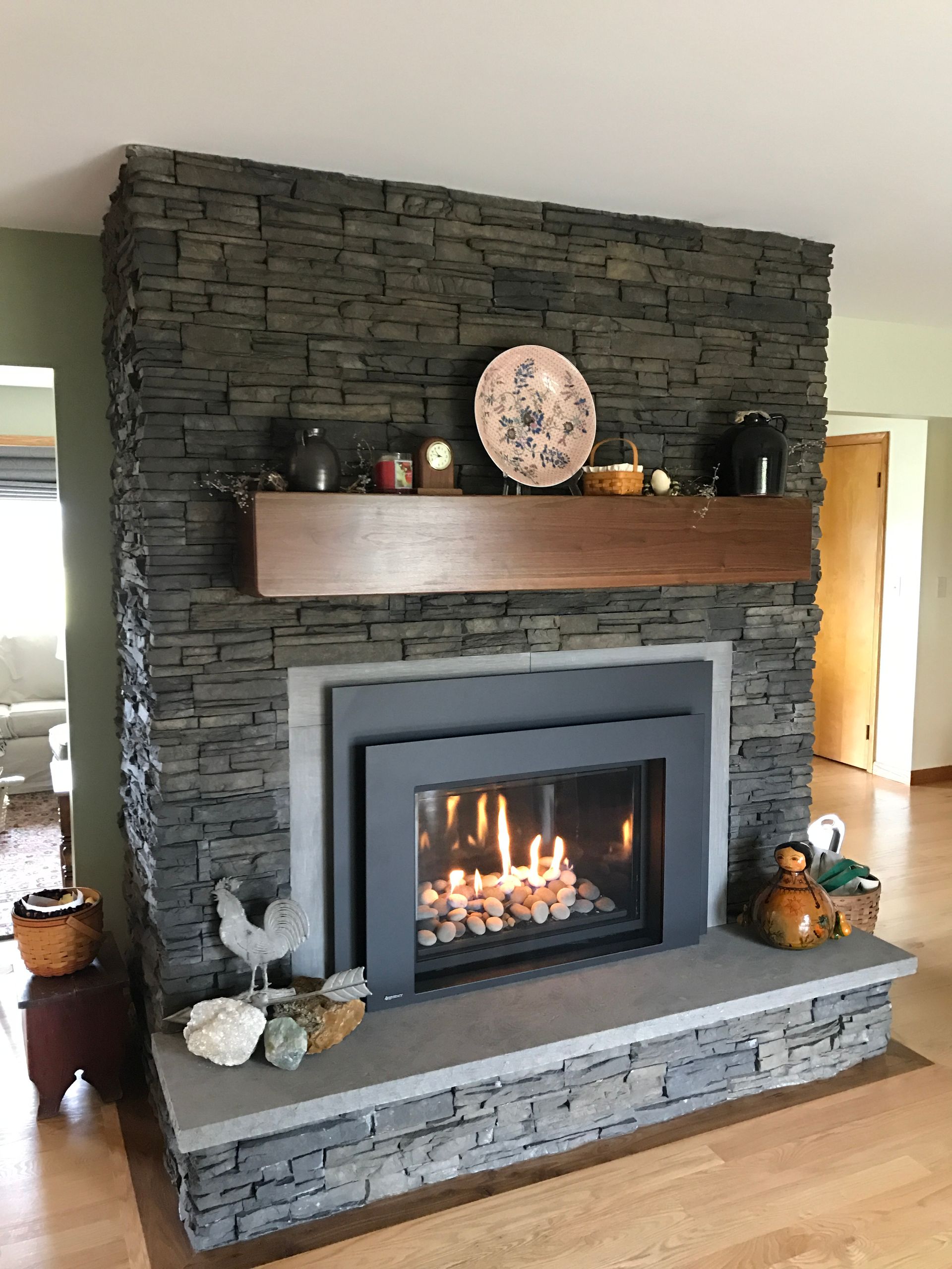 Stone fireplace with lit fire, wooden mantel, and decorative items in a living room