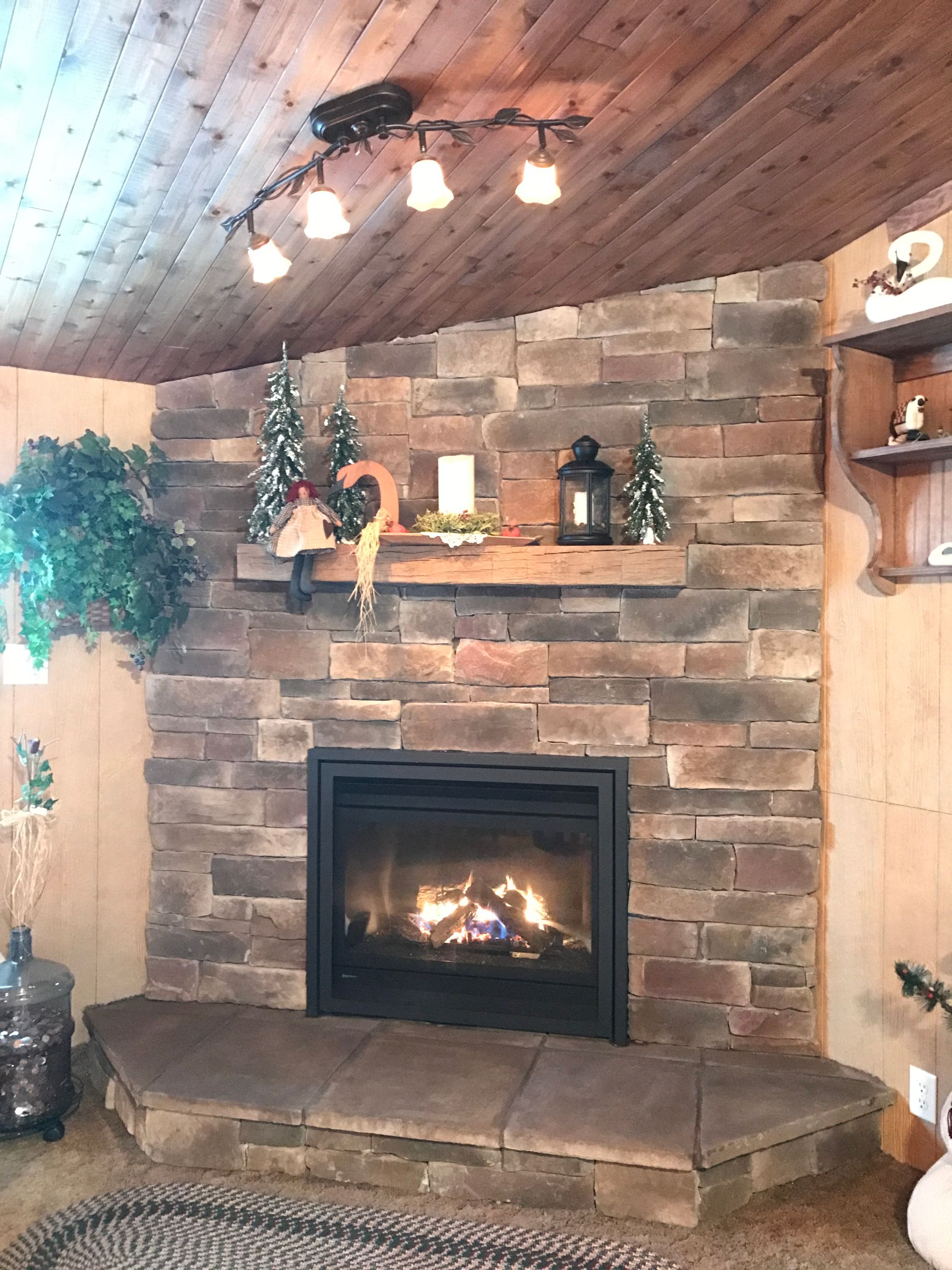 Cozy stone fireplace with a lit fire, wooden mantel, and rustic cabin-style decor.