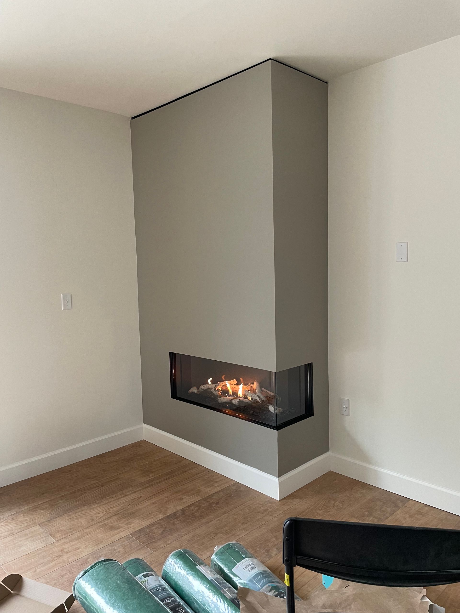 Modern room corner with a gray fireplace, light walls, and wood floor.