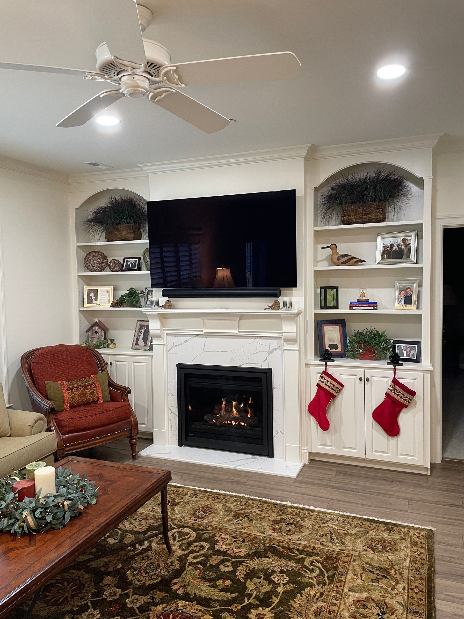 Cozy living room with fireplace, TV, built-in shelves, red stockings, and a patterned rug