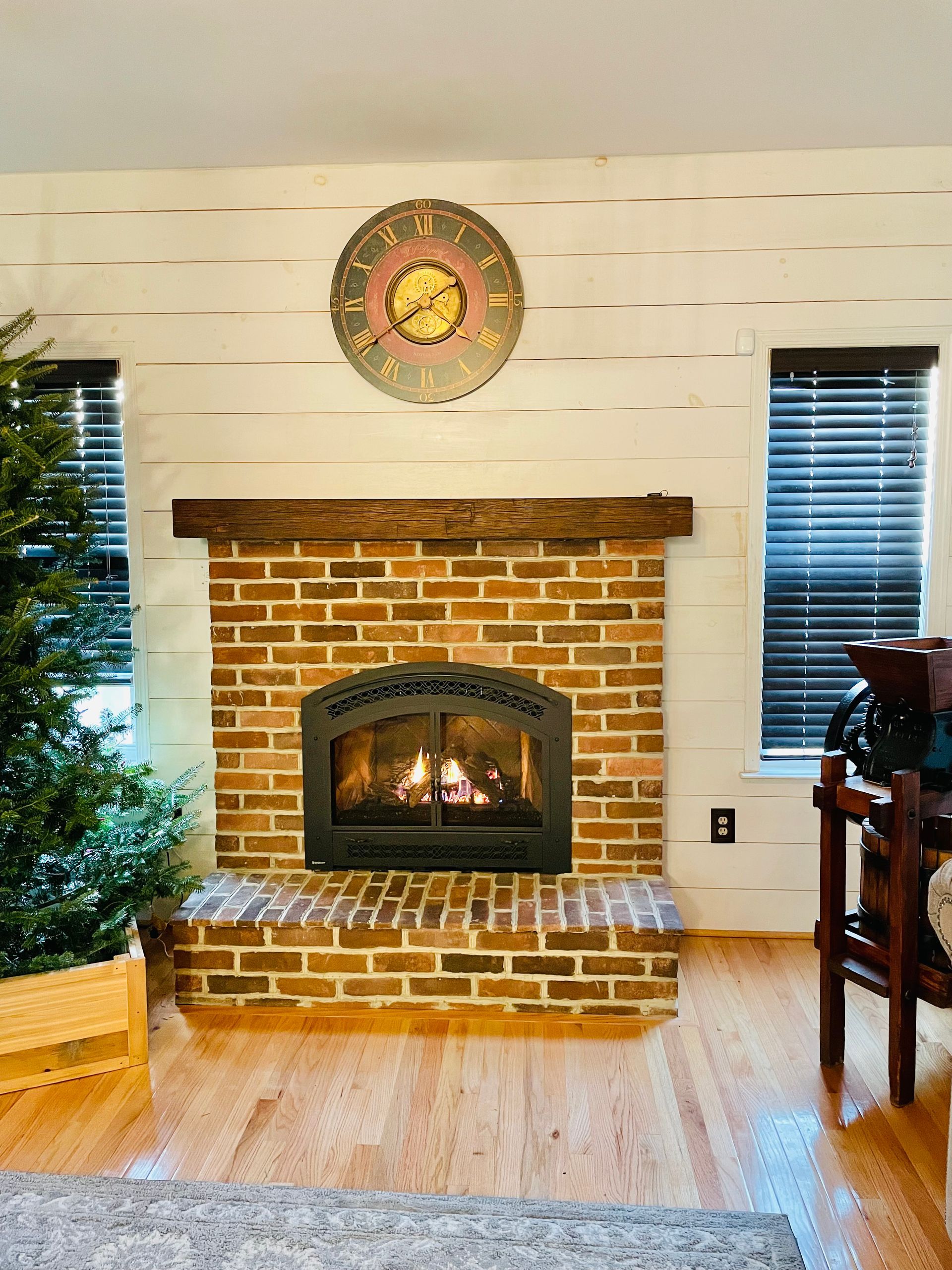 Living room with brick fireplace, lit fire, holiday tree, and window shutters