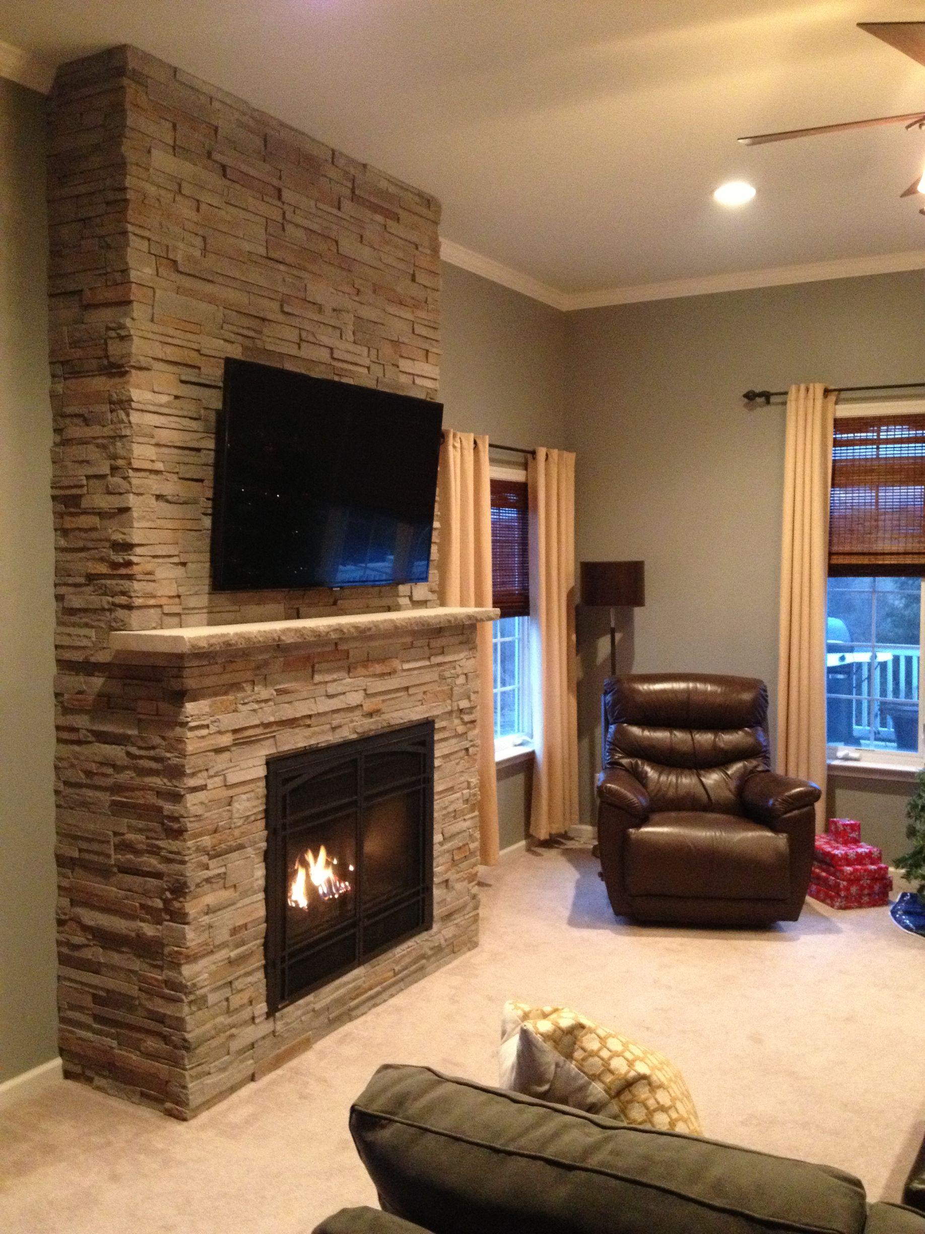 Cozy living room with stone fireplace, wall-mounted TV, recliner, and warm lighting