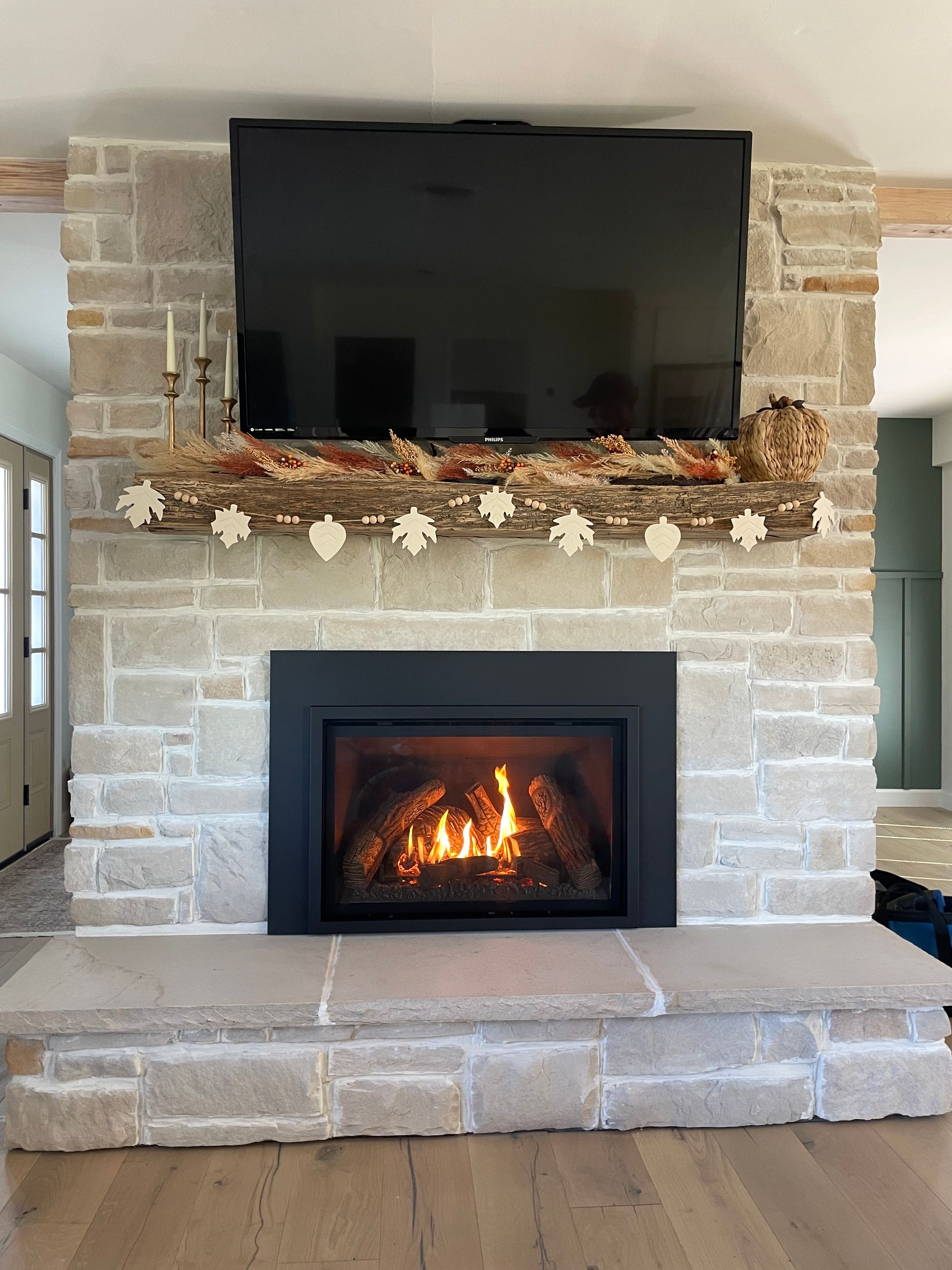 Stone fireplace with mounted TV, glowing firebox, and garland mantel in a living room