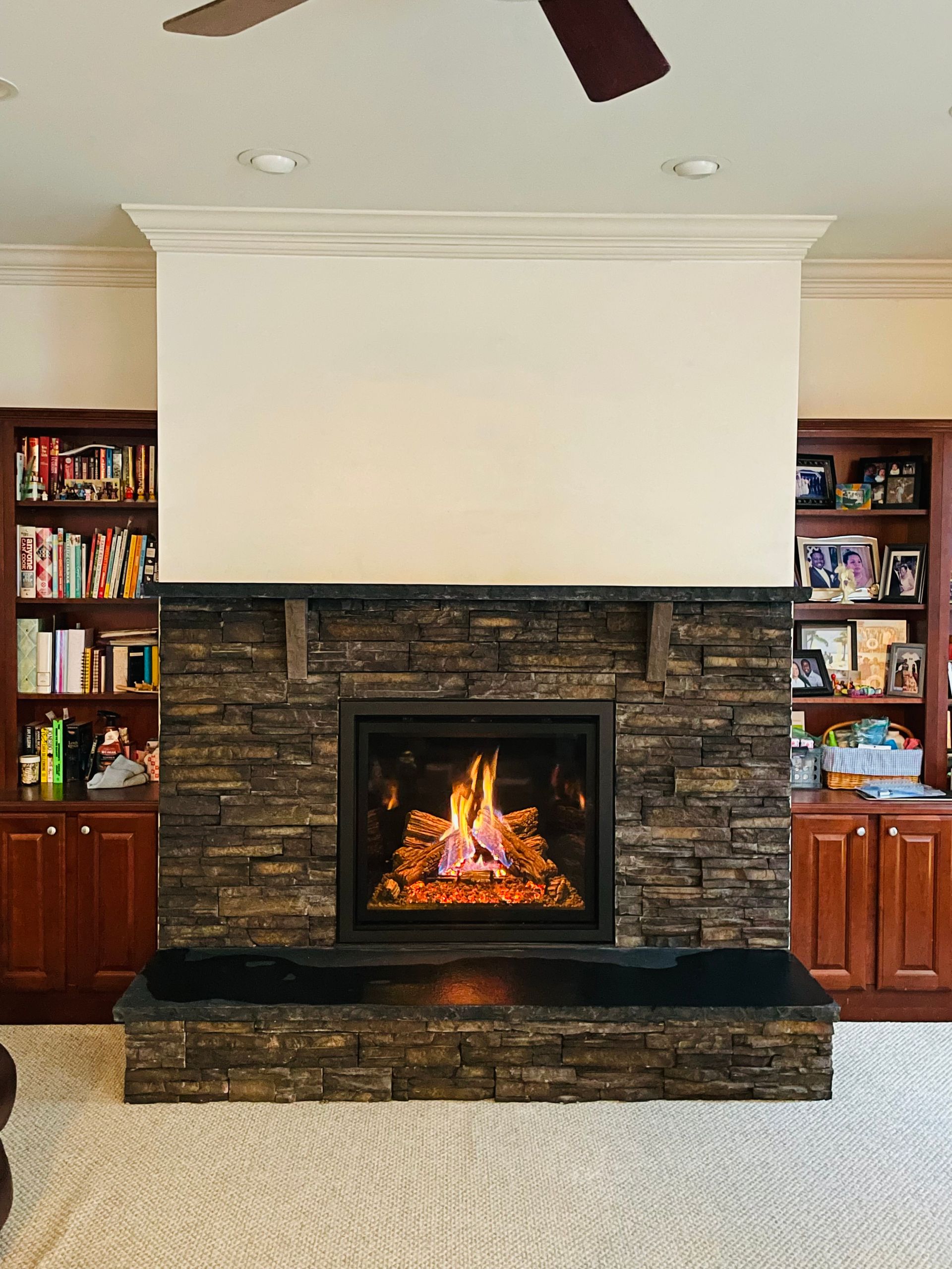Living room fireplace with stone surround, lit fire, and built-in bookshelves on both sides