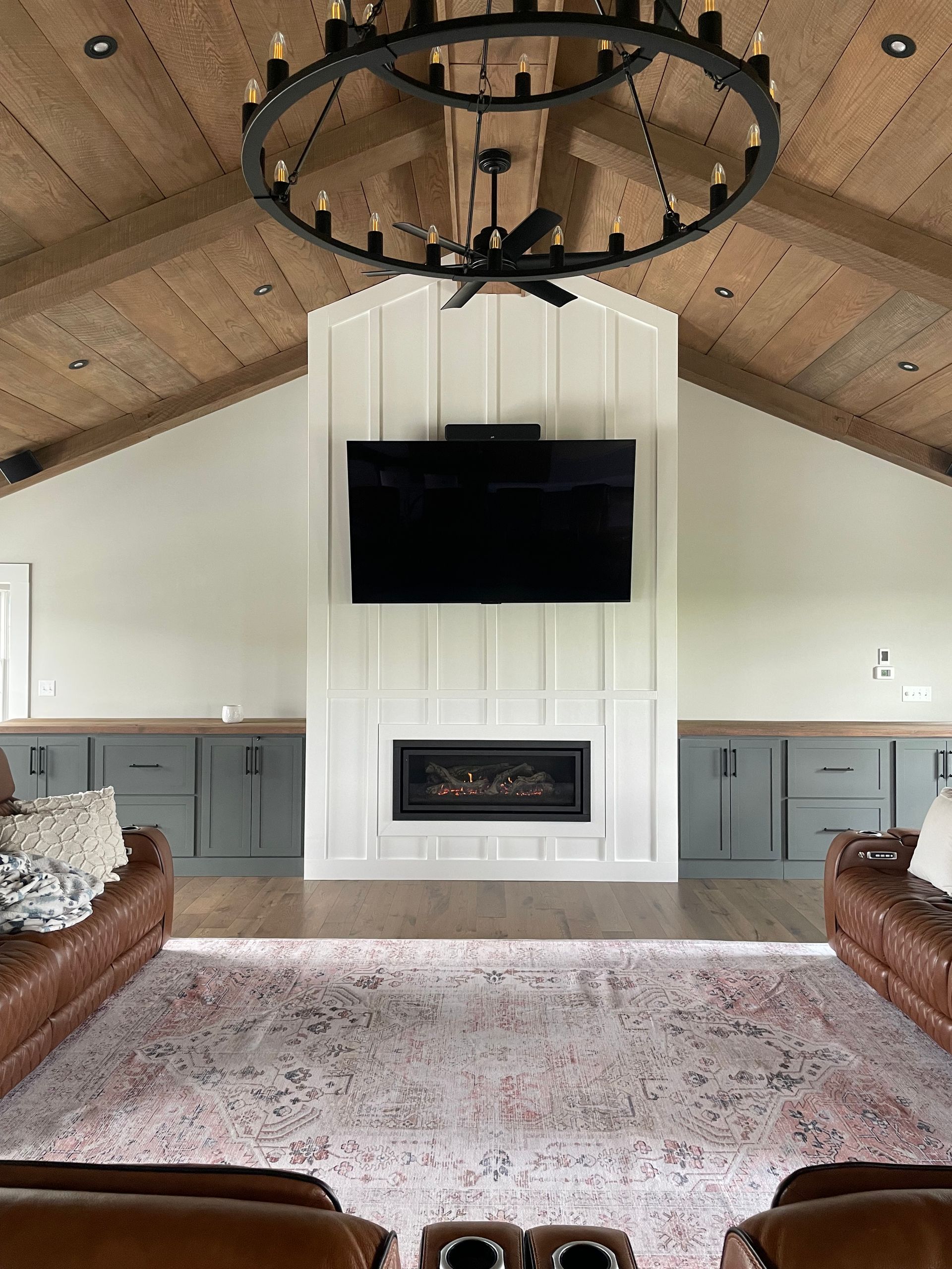 Cozy living room with vaulted wood ceiling, black chandelier, wall-mounted TV, and fireplace centered between sofas
