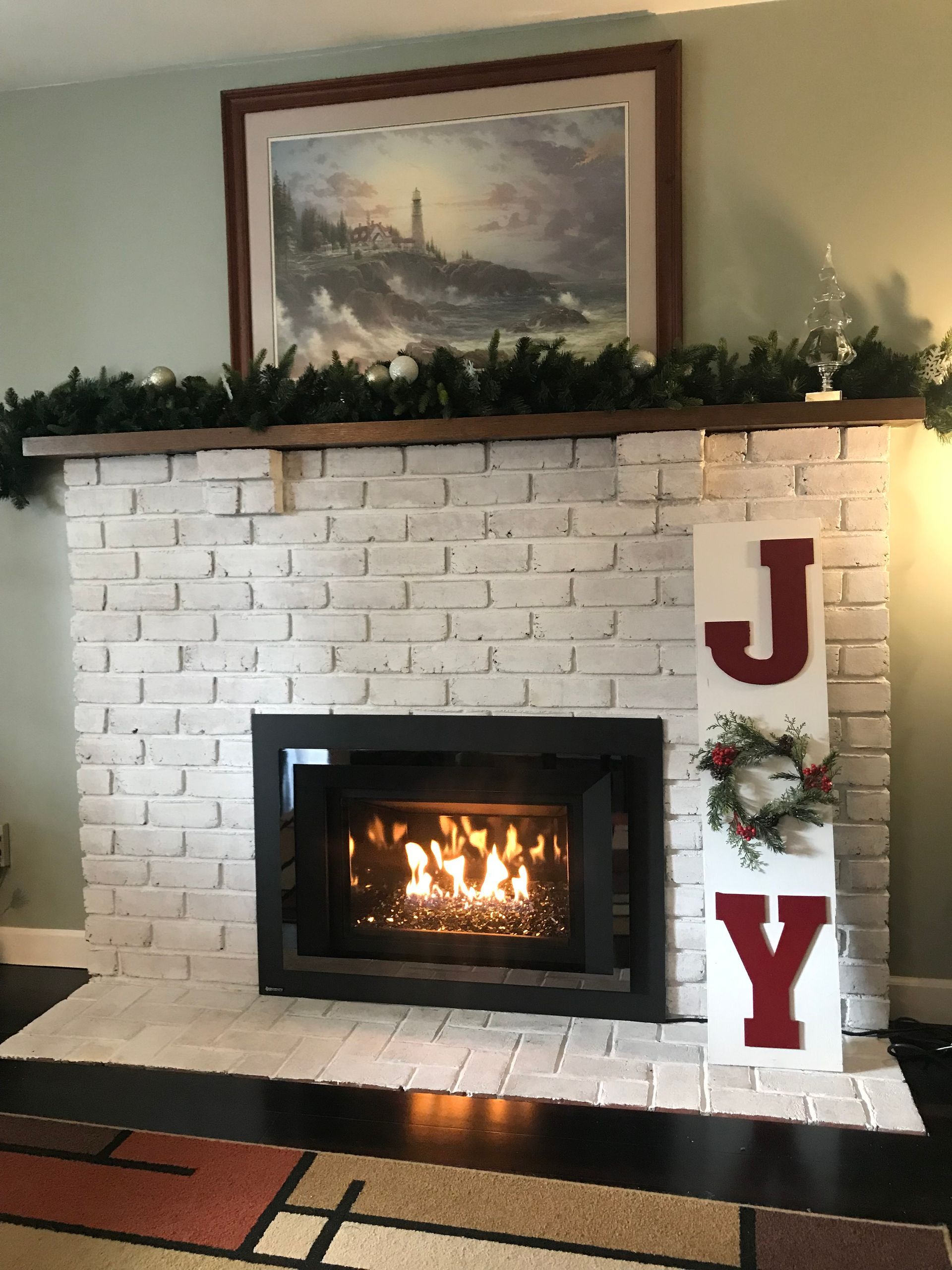 White brick fireplace with a lit fire, greenery on the mantel, and large red holiday letters J and Y.