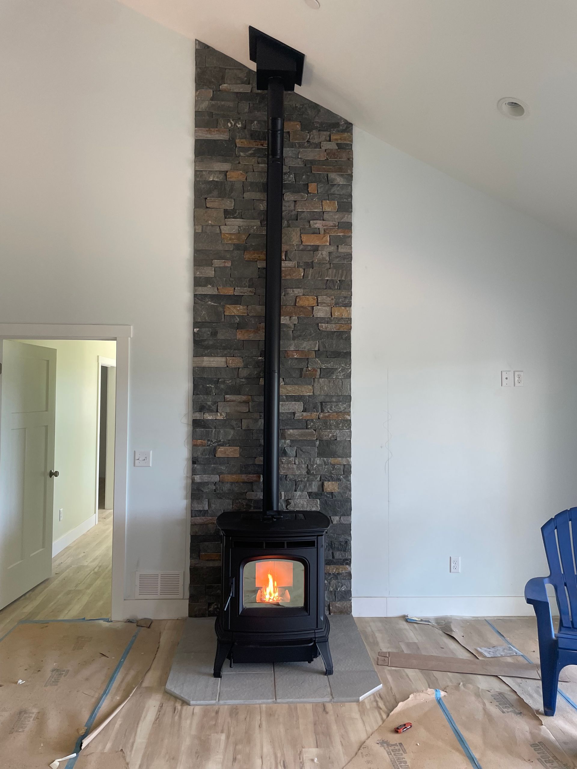 Living room with a lit wood stove and tall stone chimney on a white wall, with a doorway at left.