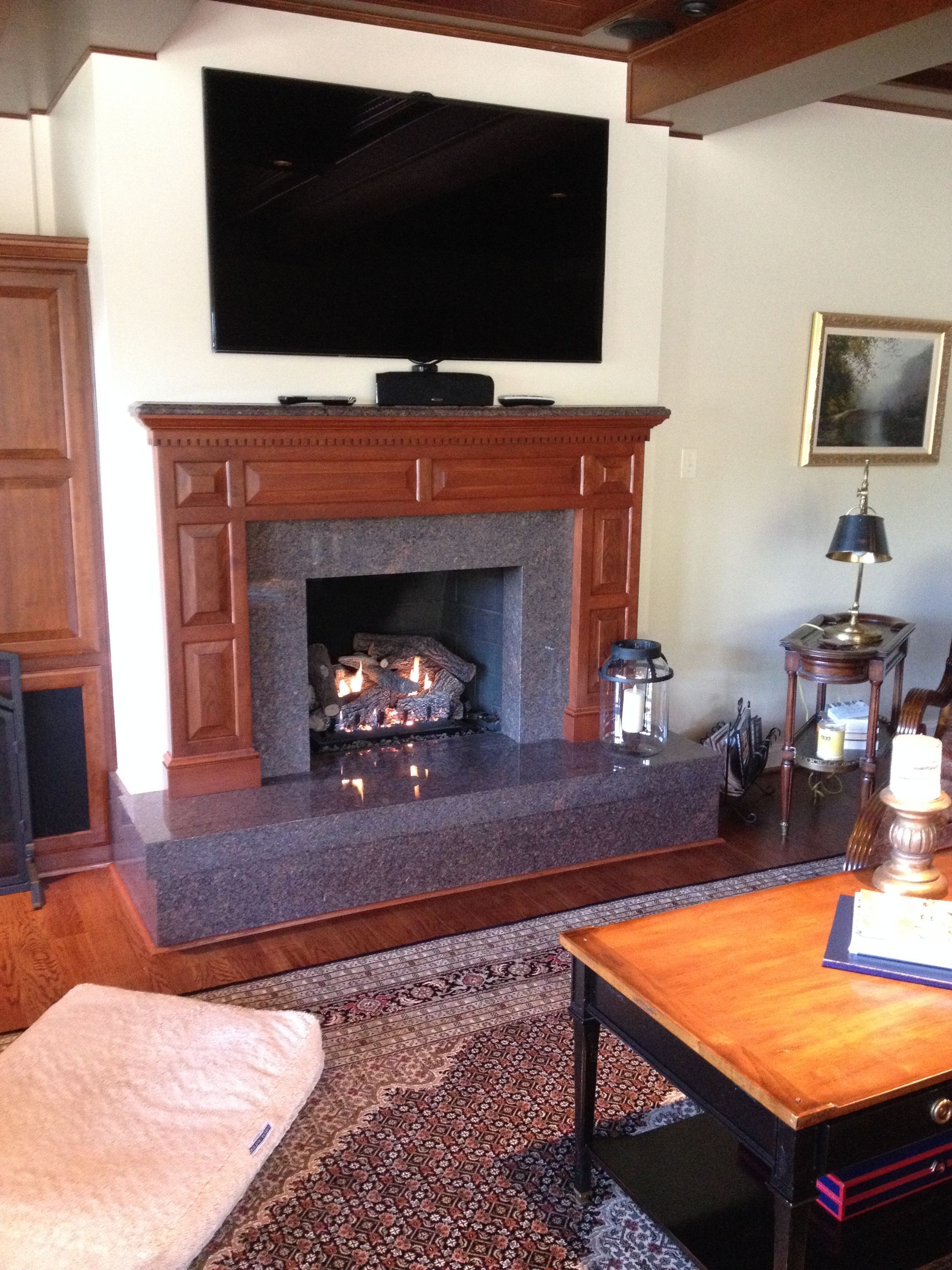 Cozy living room with lit fireplace, wall-mounted TV, and wooden mantel under a sloped ceiling.