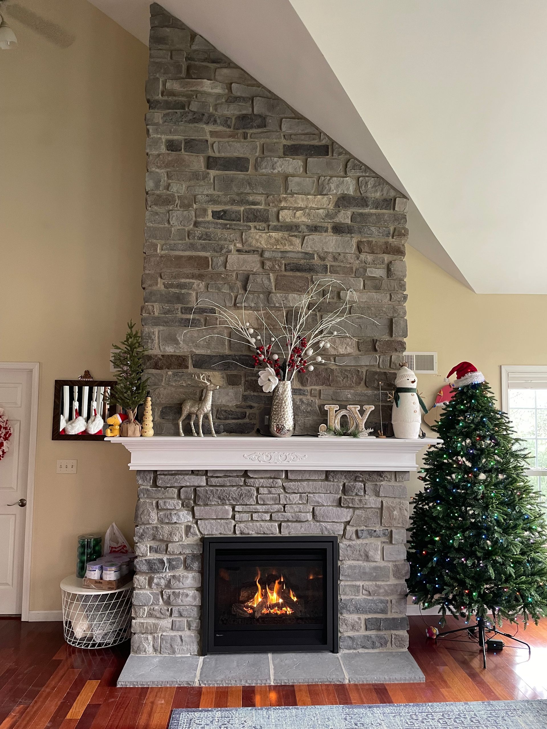 Stone fireplace with lit fire, Christmas decorations, and a small lit tree in a cozy living room.