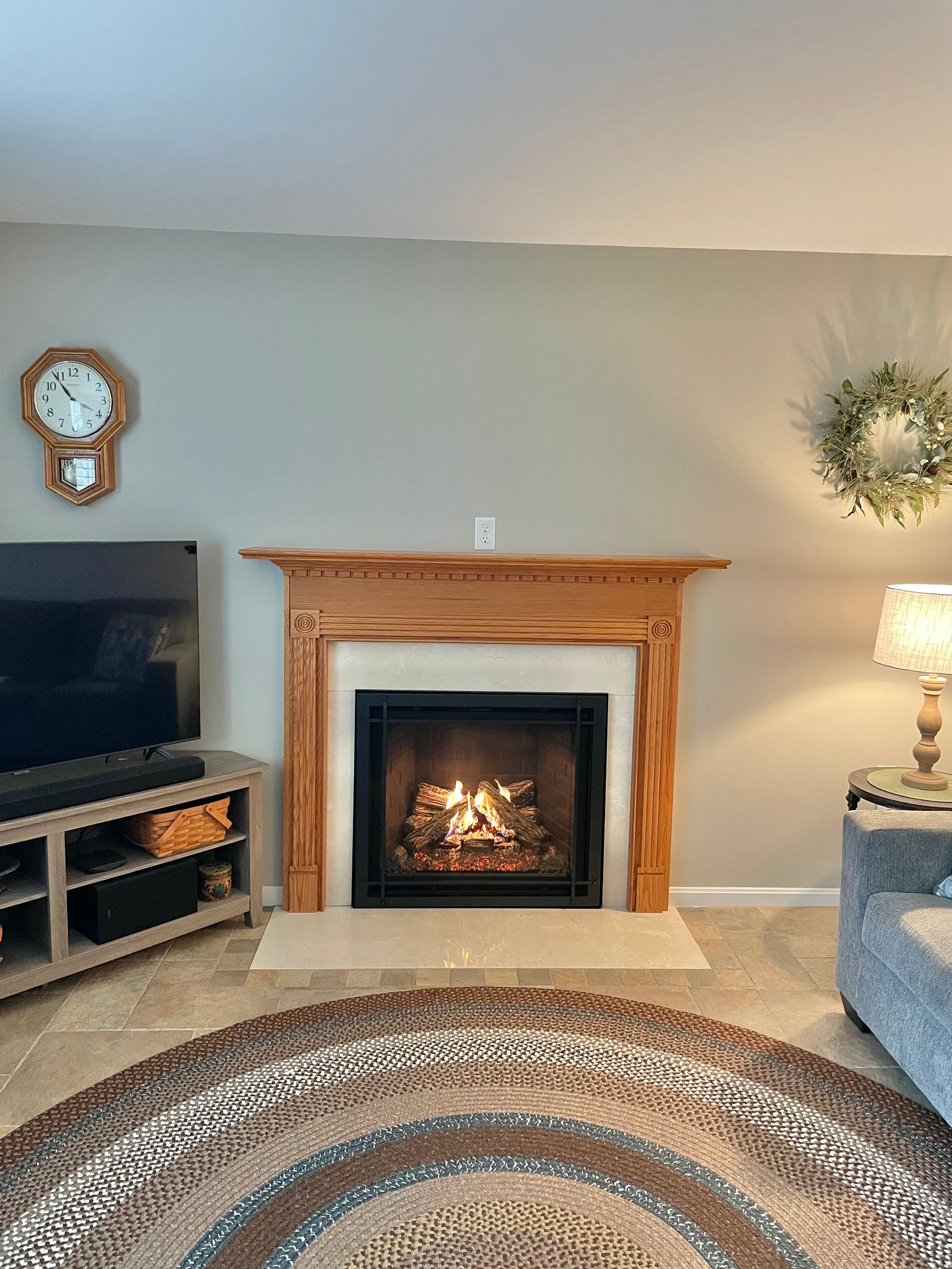 Living room with lit fireplace, TV, patterned rug, and lamp beside a gray sofa