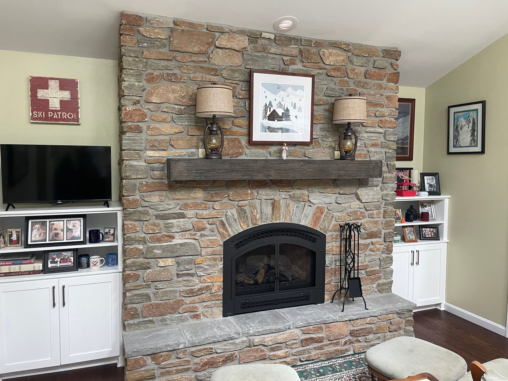 Living room with stone fireplace, mantel decor, wall-mounted TV, and white cabinets on either side