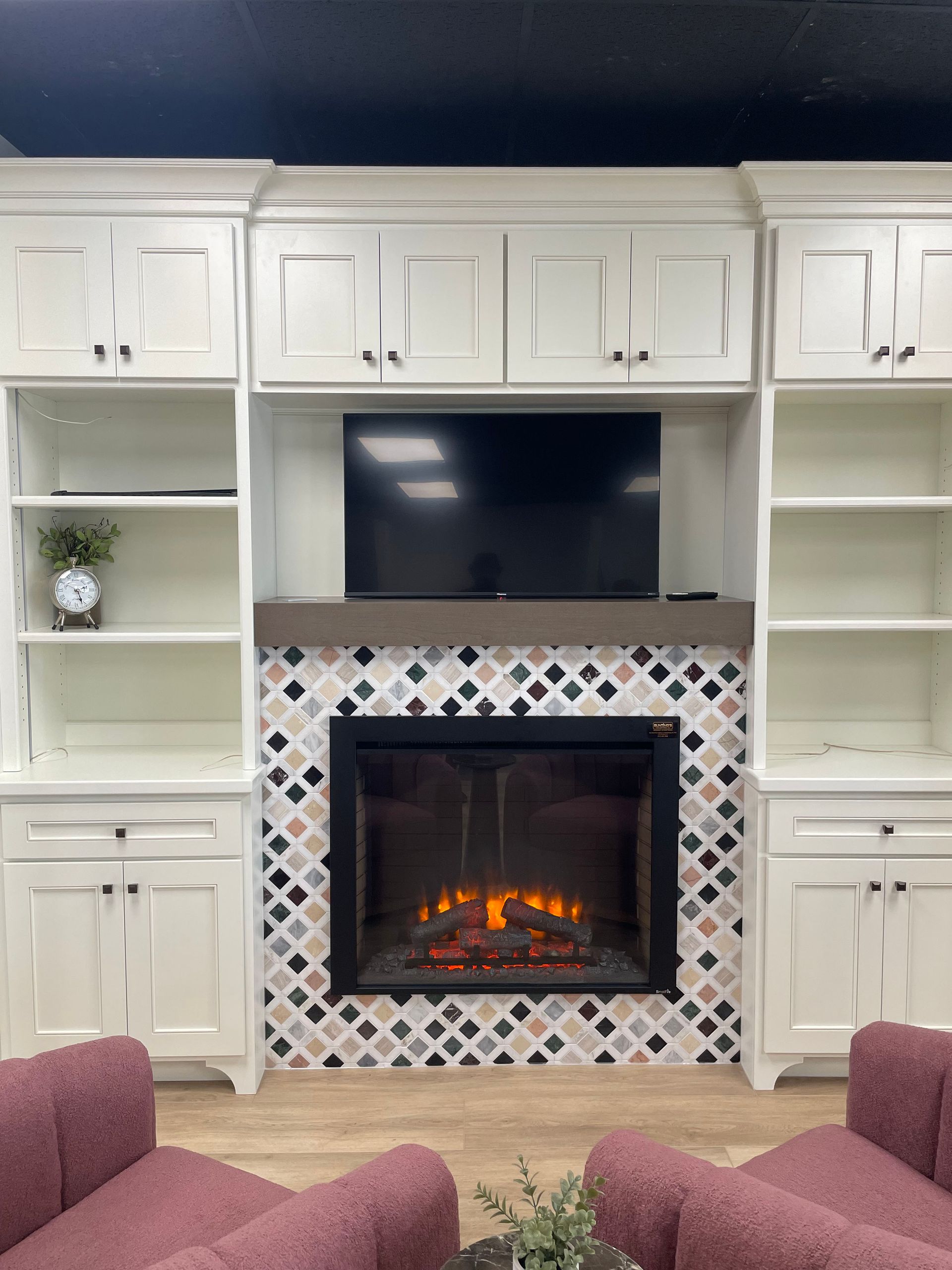 Built-in white living room cabinets framing a TV and lit fireplace with patterned tile surround