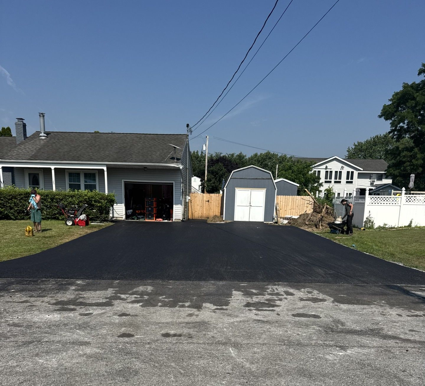 Freshly paved black driveway leading to a gray garage and house on a sunny residential street