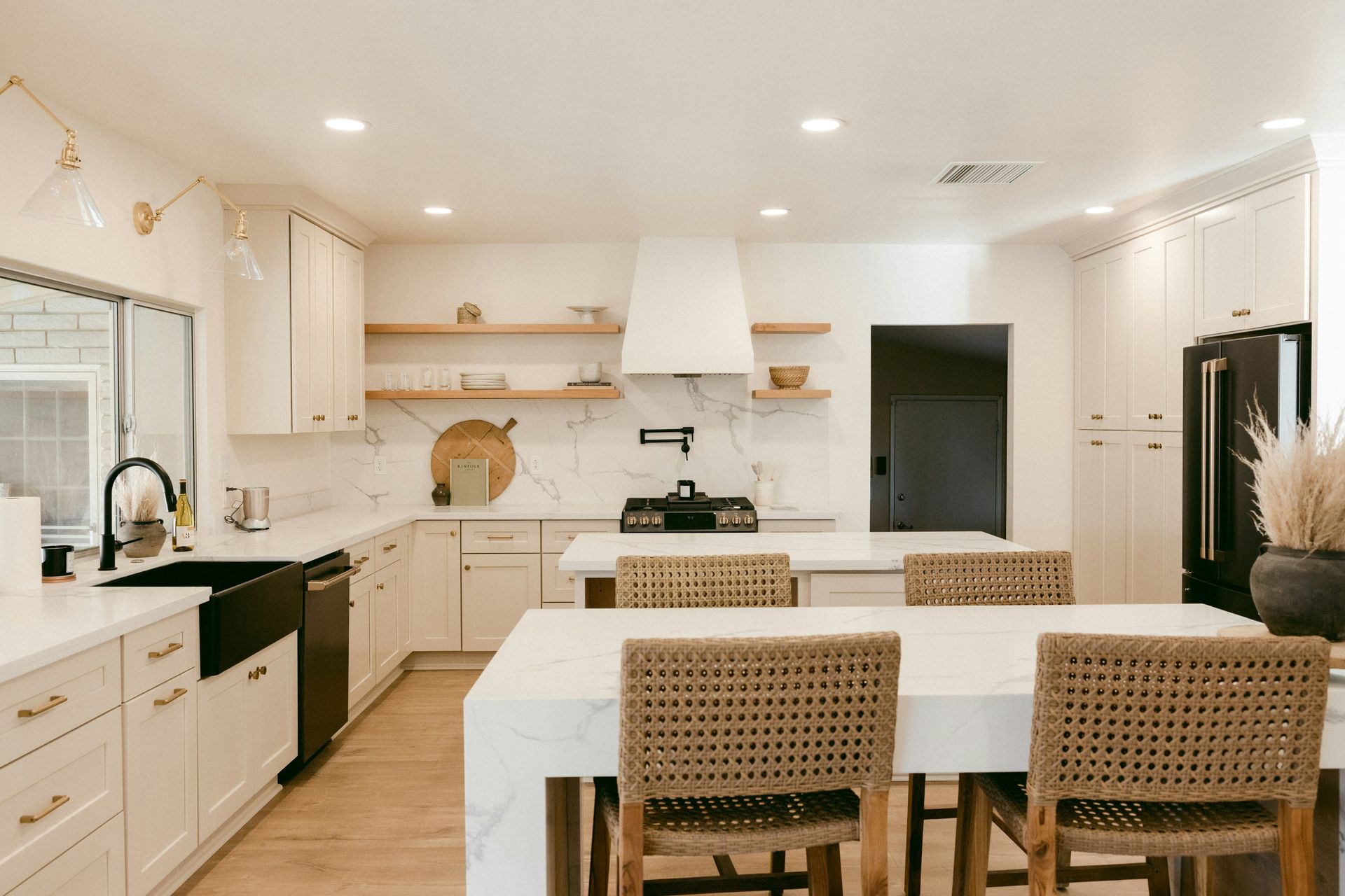 a kitchen with white cabinets, a large island, a sink and wicker chairs