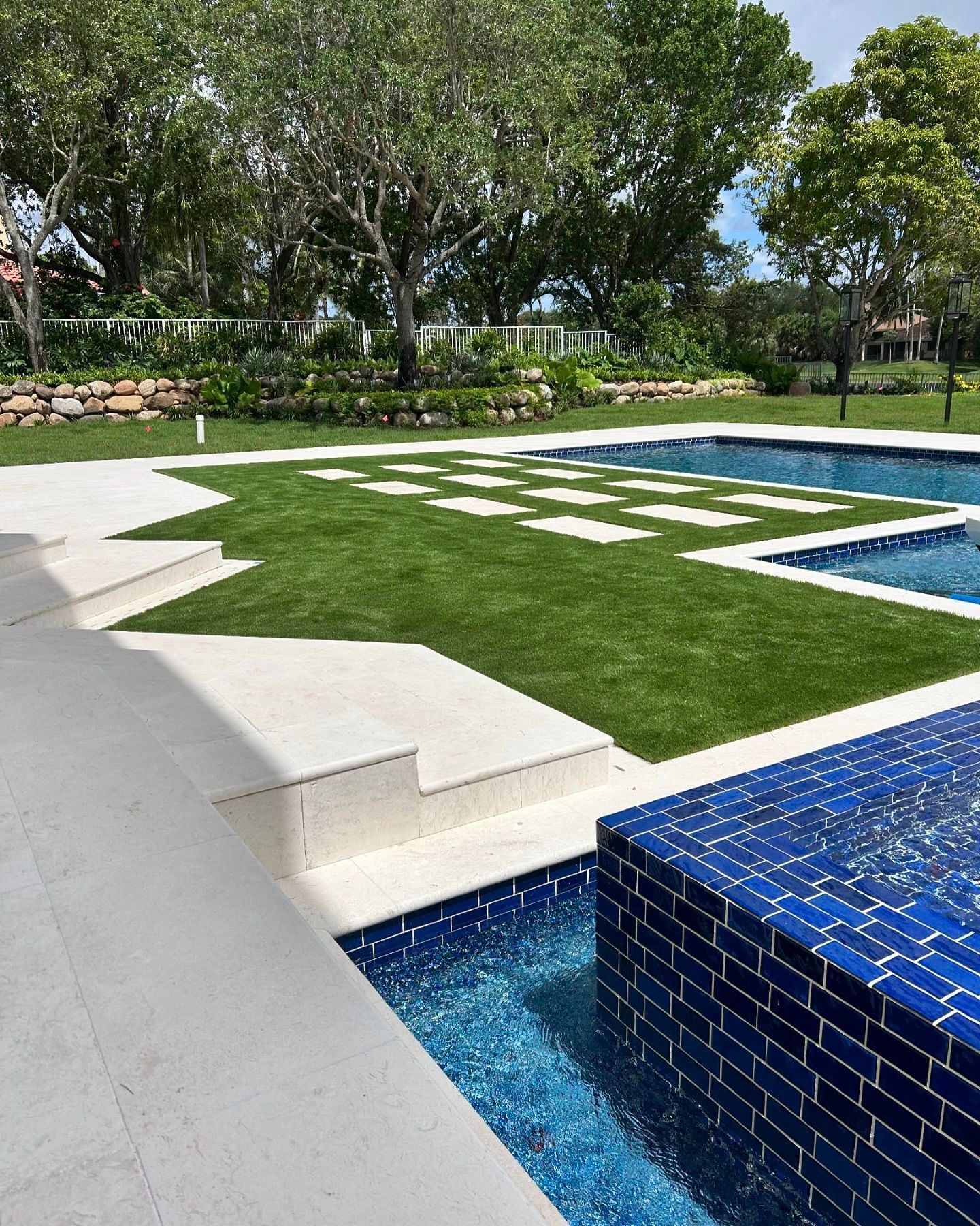 A large swimming pool surrounded by a lush green lawn and trees.