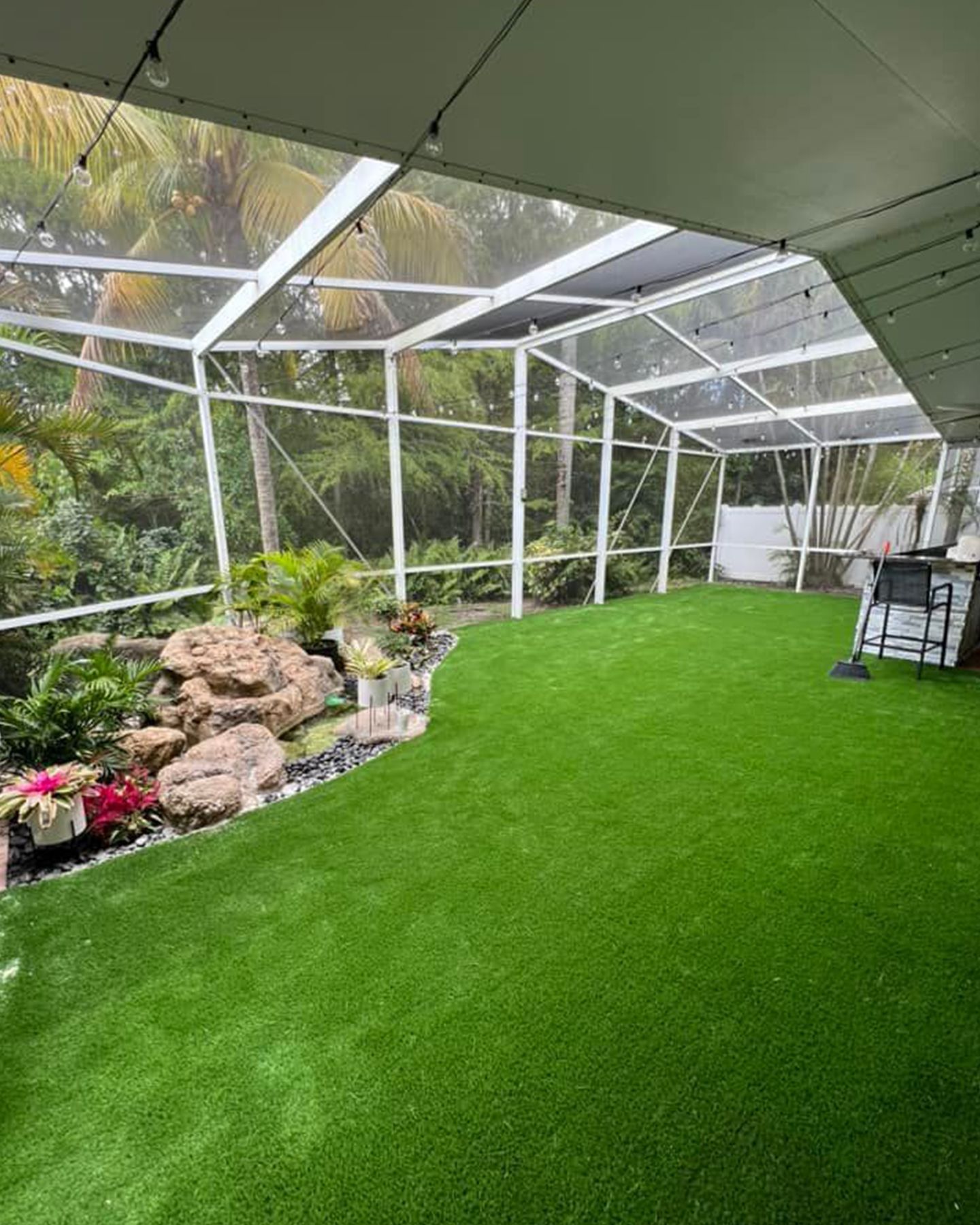 A screened in porch with a lot of green grass and rocks.