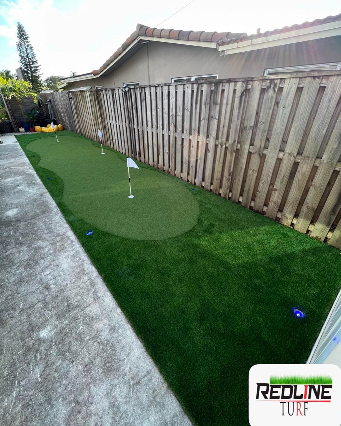 A backyard with a putting green and a wooden fence.