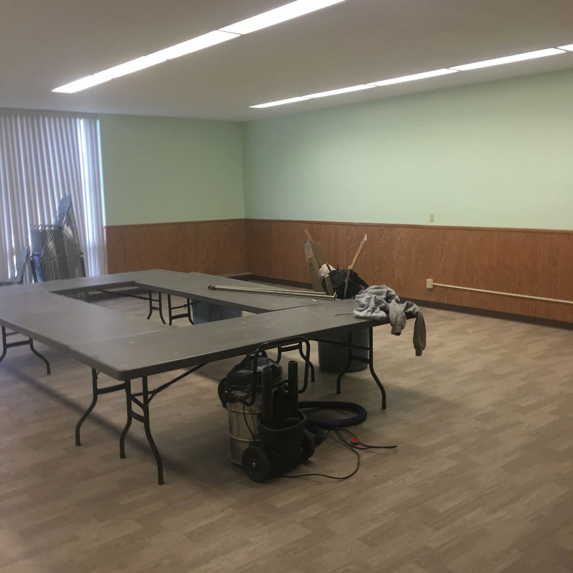 Empty conference room with long tables, folding chairs, and scattered equipment on the floor.