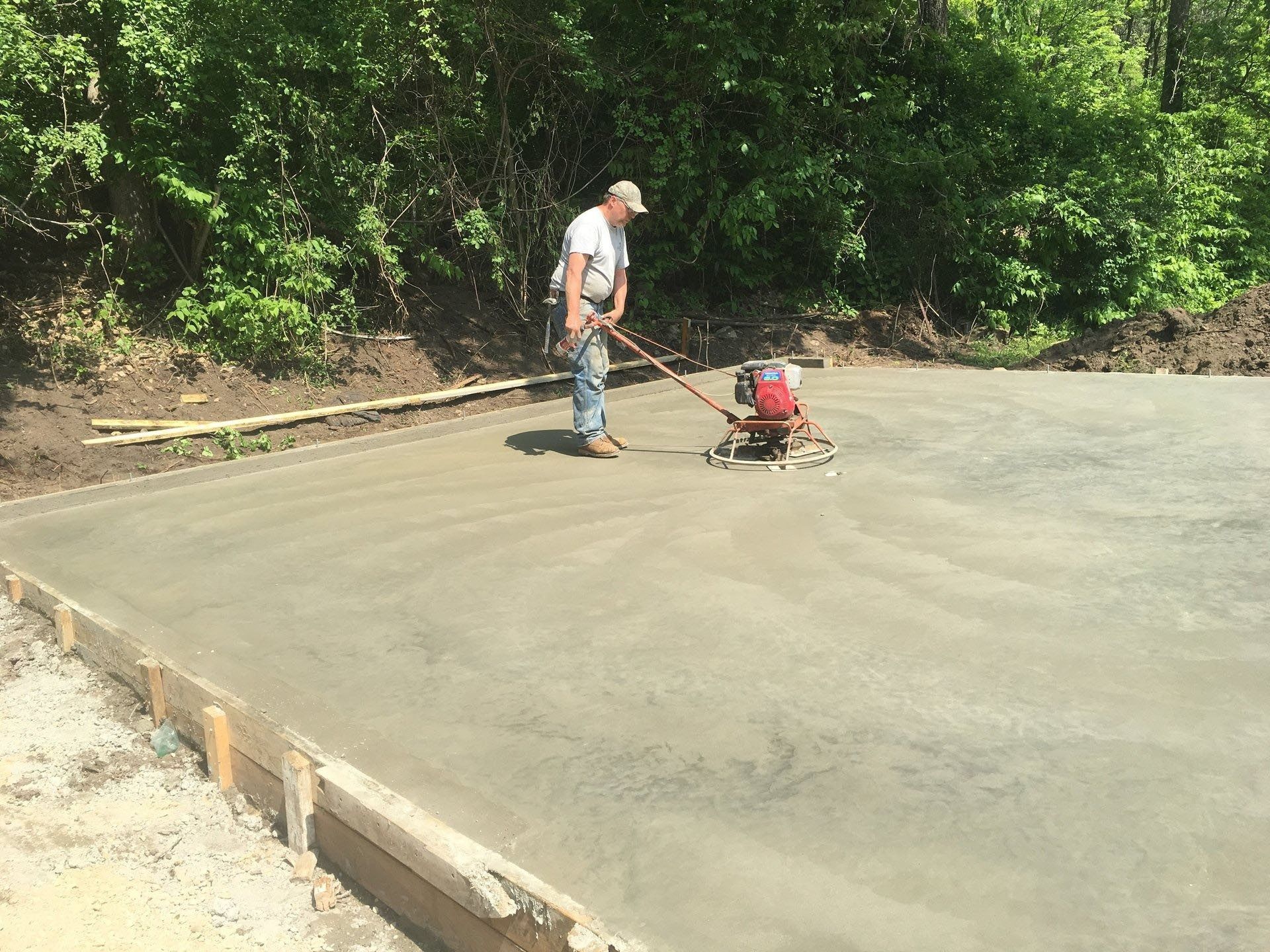 Worker using a power trowel to smooth fresh concrete on a slab at a construction site