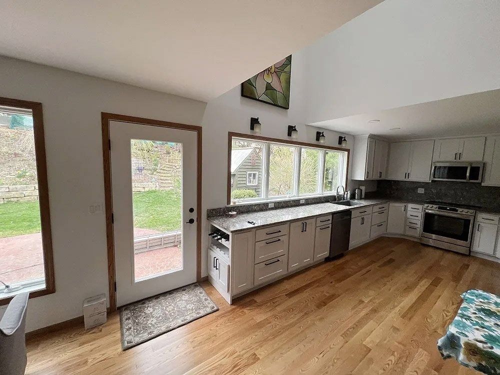 Bright kitchen with wood floors, white cabinets, stainless appliances, and a glass door to outside.