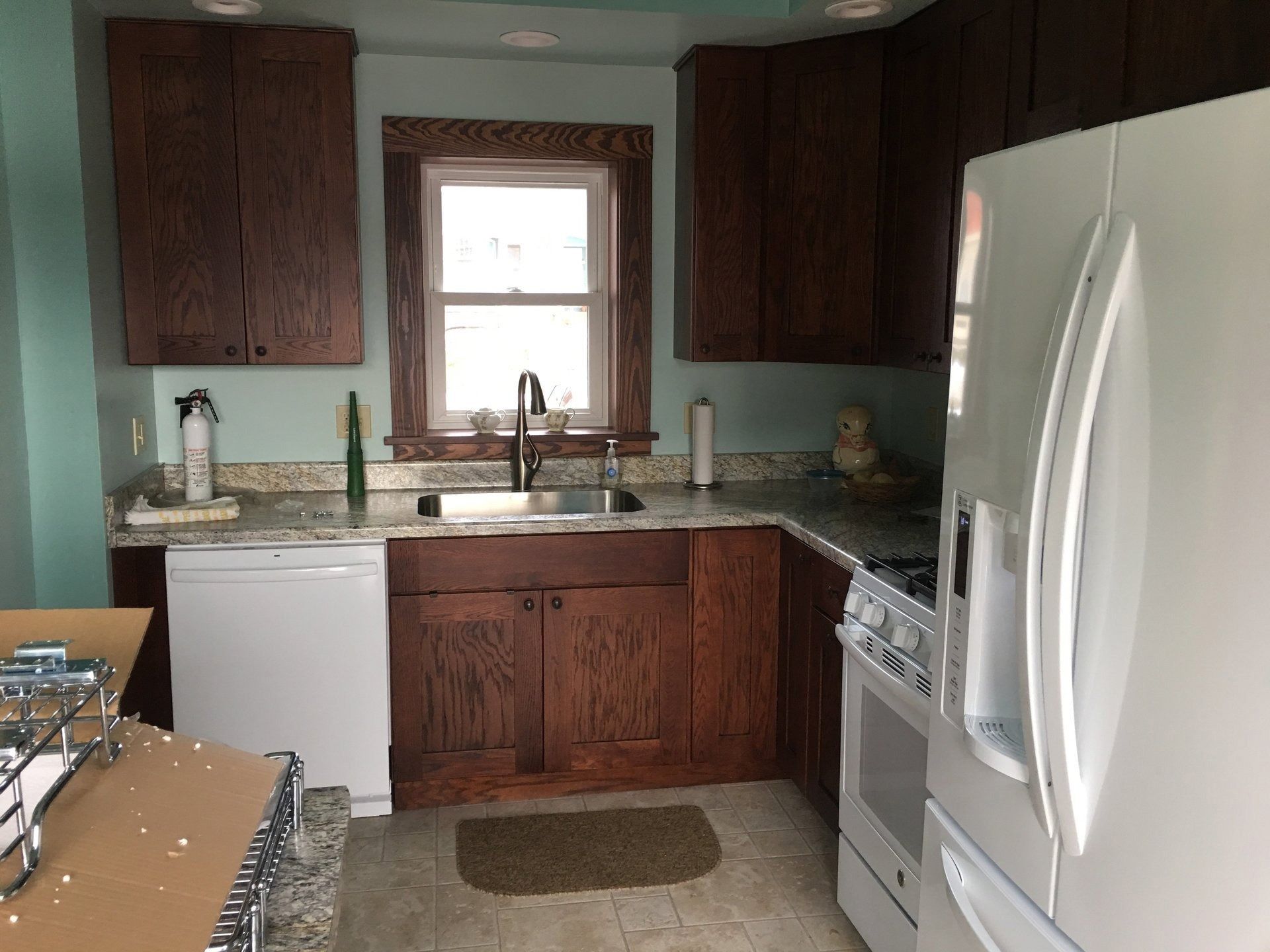 Small kitchen with white appliances, dark wood cabinets, and a window above the sink.