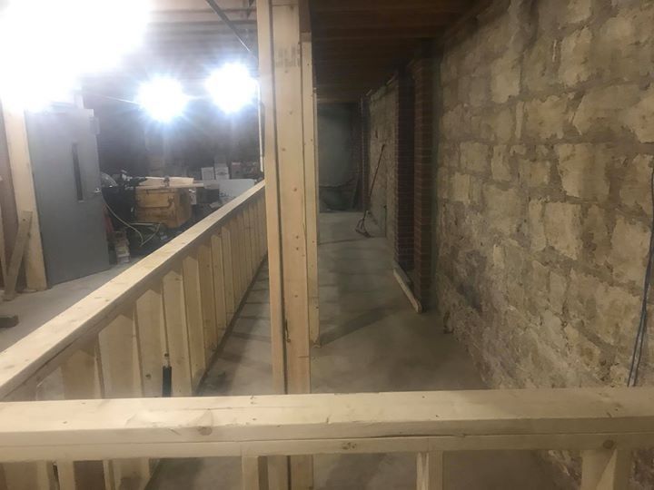Dim unfinished corridor with wooden railings, stone wall, and bright lights in a construction area