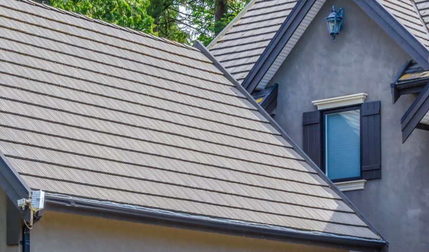 Gray house roof with blue-gray siding and a window under tree-covered sky