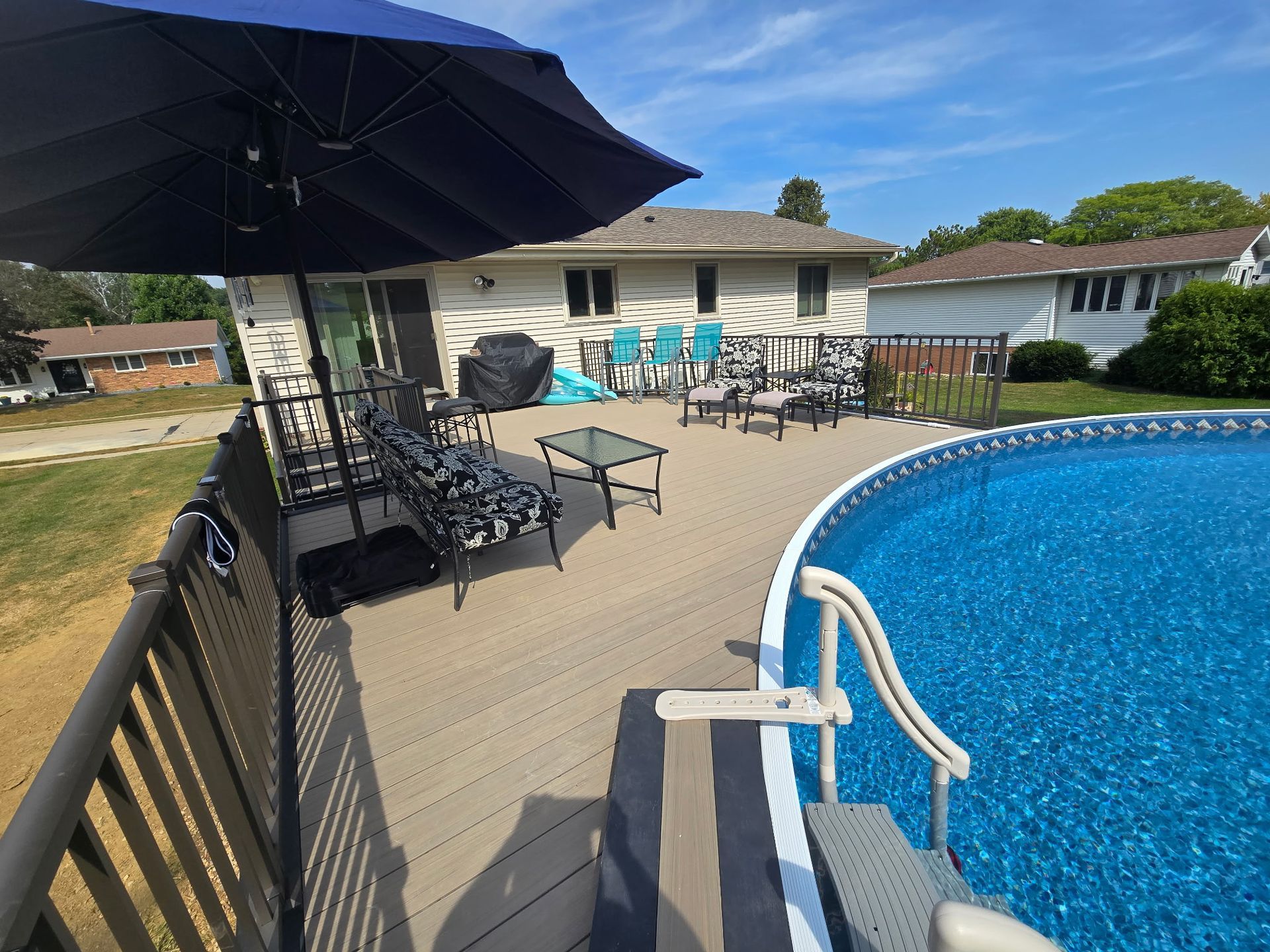 Backyard pool deck with black umbrella, lounge chairs, and blue swimming pool