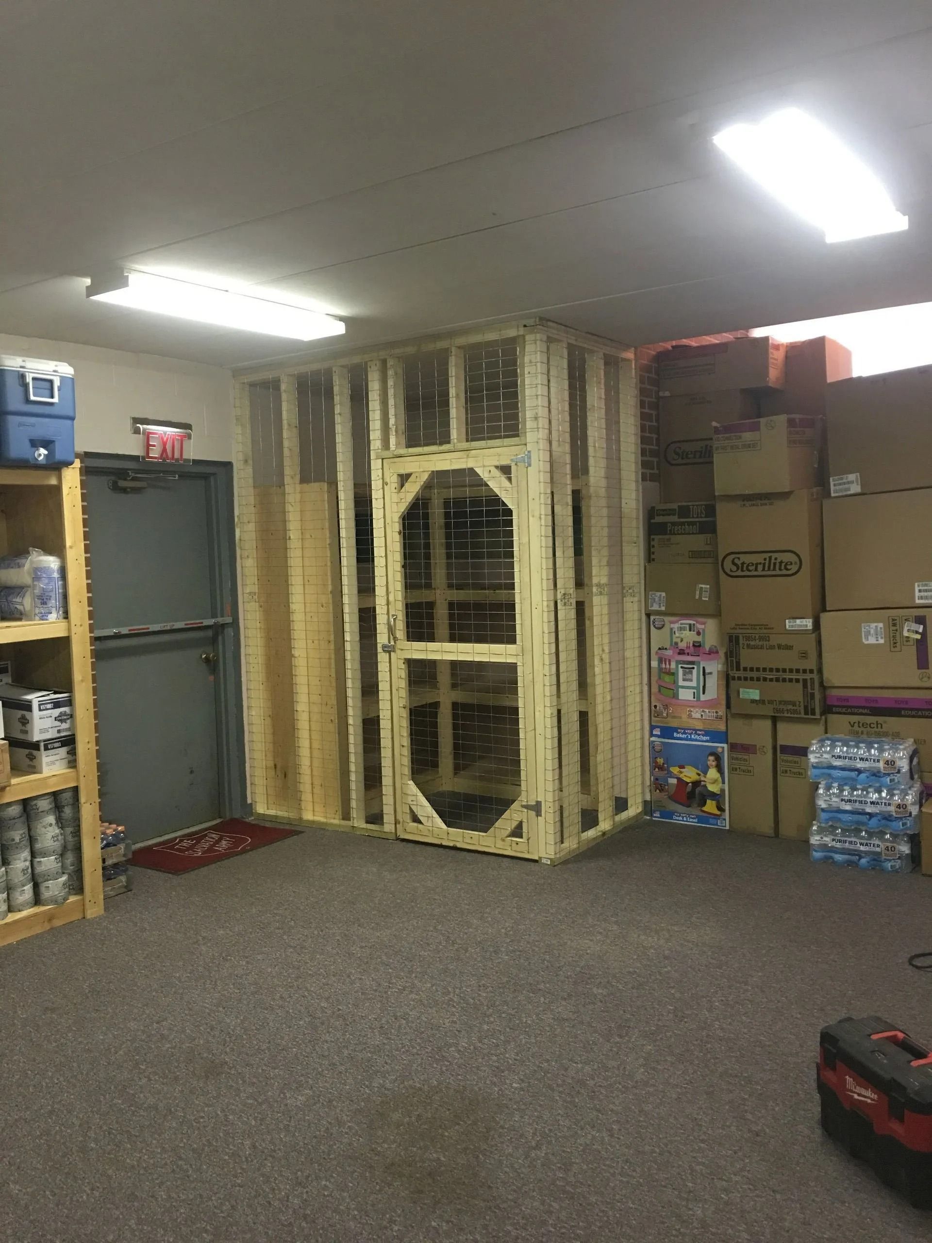 Storage room with stacked boxes, shelves, and a large framed wall opening wrapped in plastic.