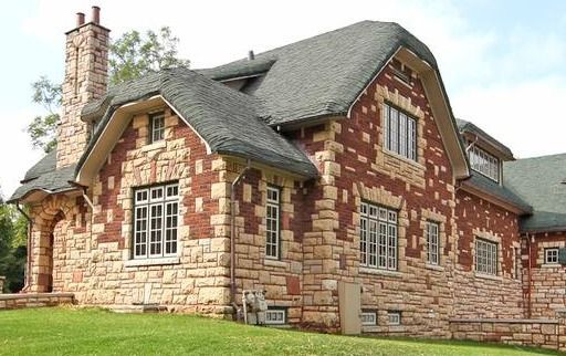 Stone house with red brick accents, gray shingled roof, and large windows on a grassy lawn