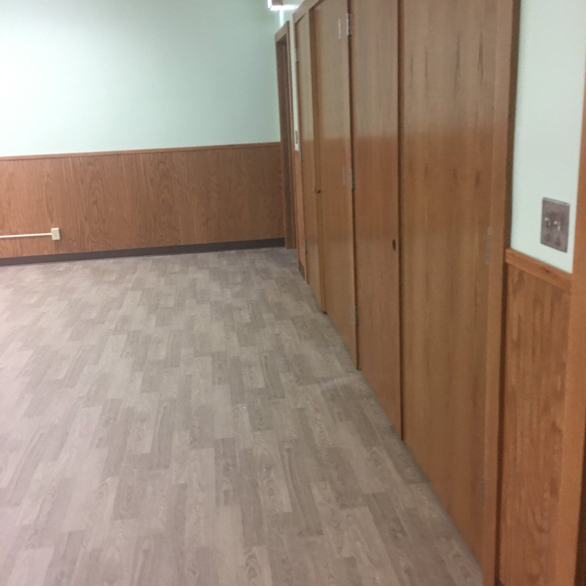 Empty hallway with wood-paneled walls, gray flooring, and closed wooden doors