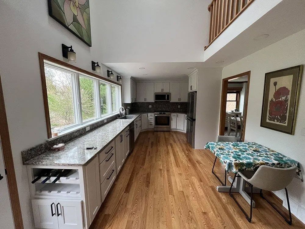 Bright kitchen with long granite counters, wood floor, and a small table by the window.