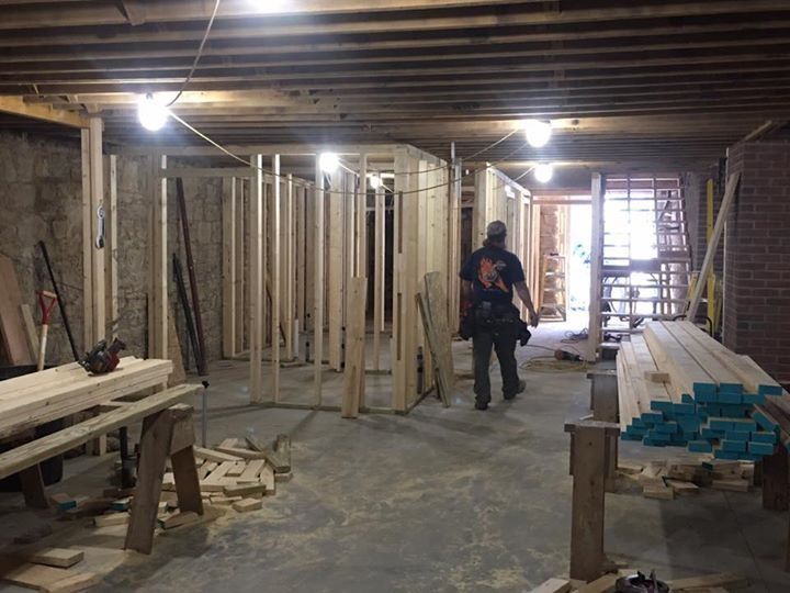 Construction site interior with unfinished walls, exposed beams, and one worker standing in the center.