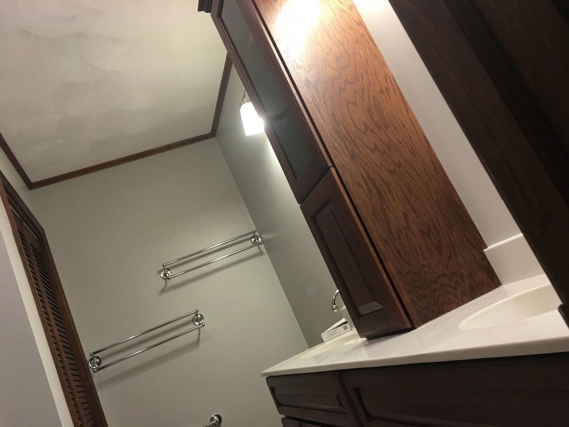 Bathroom vanity with a tilted mirror, white countertop, and wall-mounted towel racks.