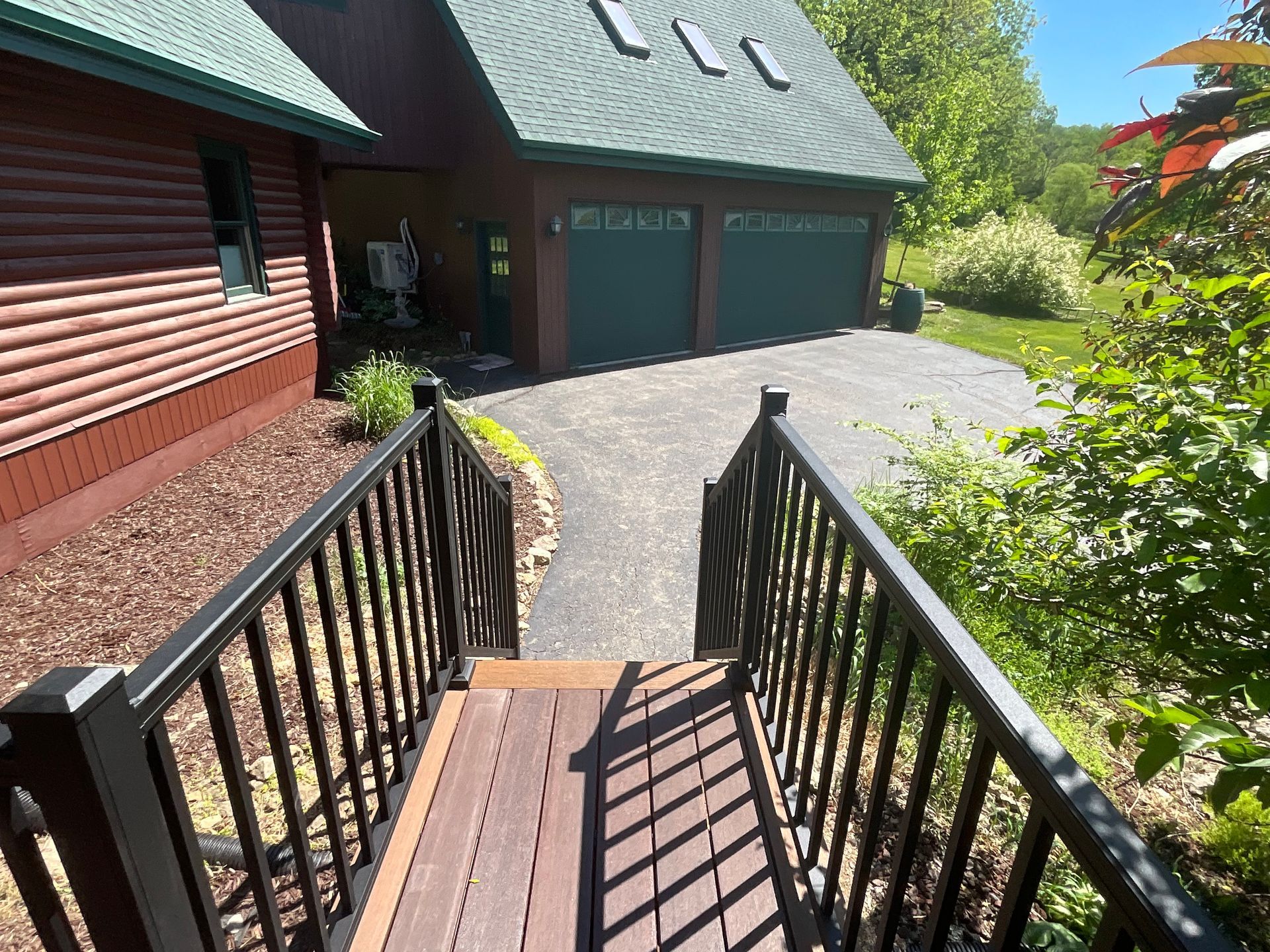 Front porch ramp with black railings leading to a brick house and green garage doors on a sunny day
