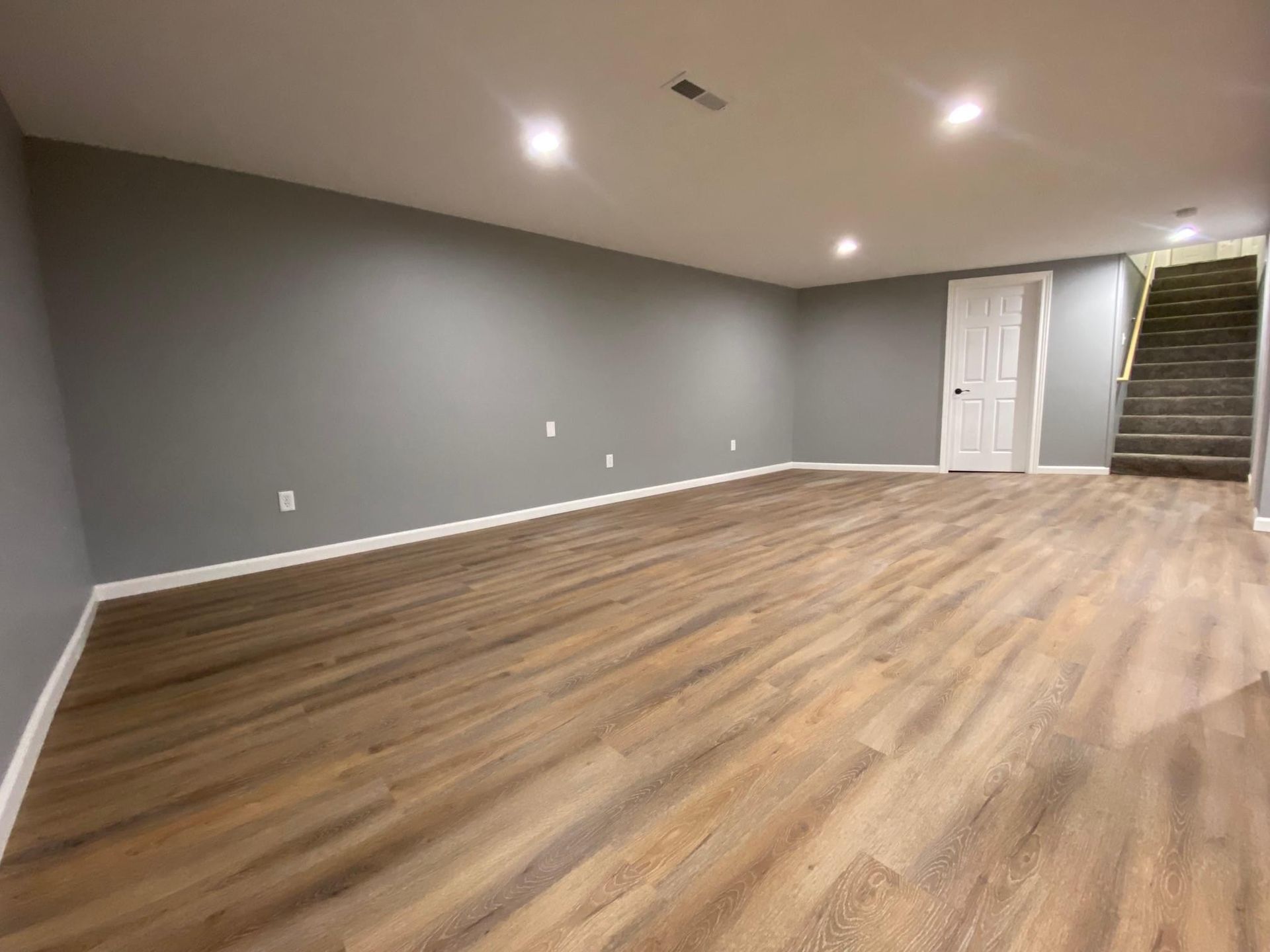 Empty room with gray walls, wood floor, recessed lights, and stairs by a doorway