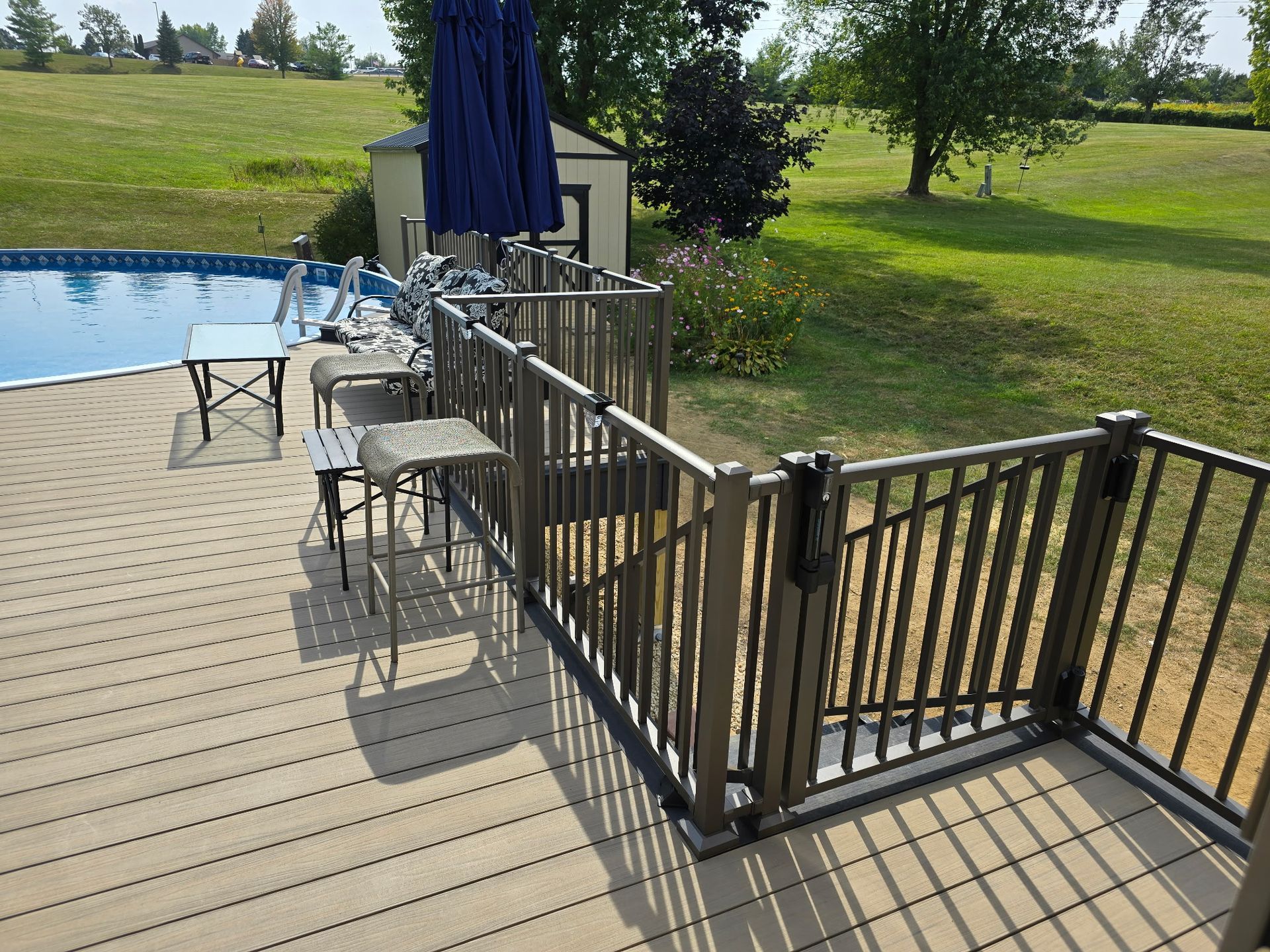 Patio deck with metal railings, blue umbrellas, and chairs beside a grassy park and pond