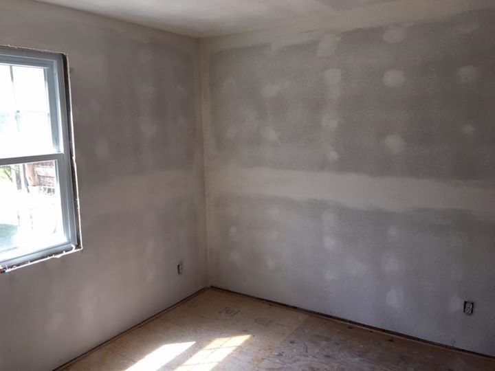Empty room with gray drywall, a window on the left, and bare floor.