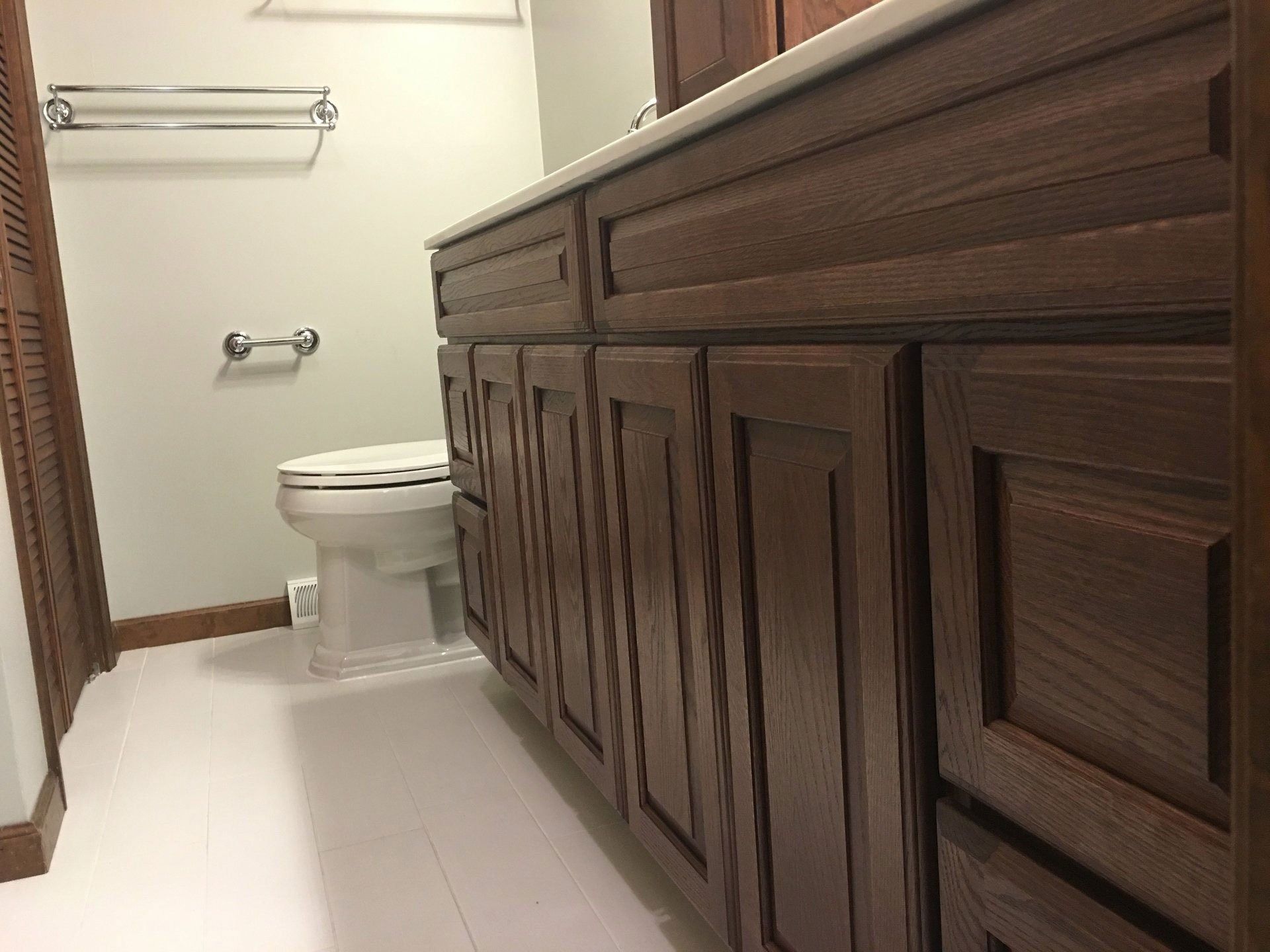 Bathroom with white tile floor, toilet, towel bars, and dark wood vanity cabinets.