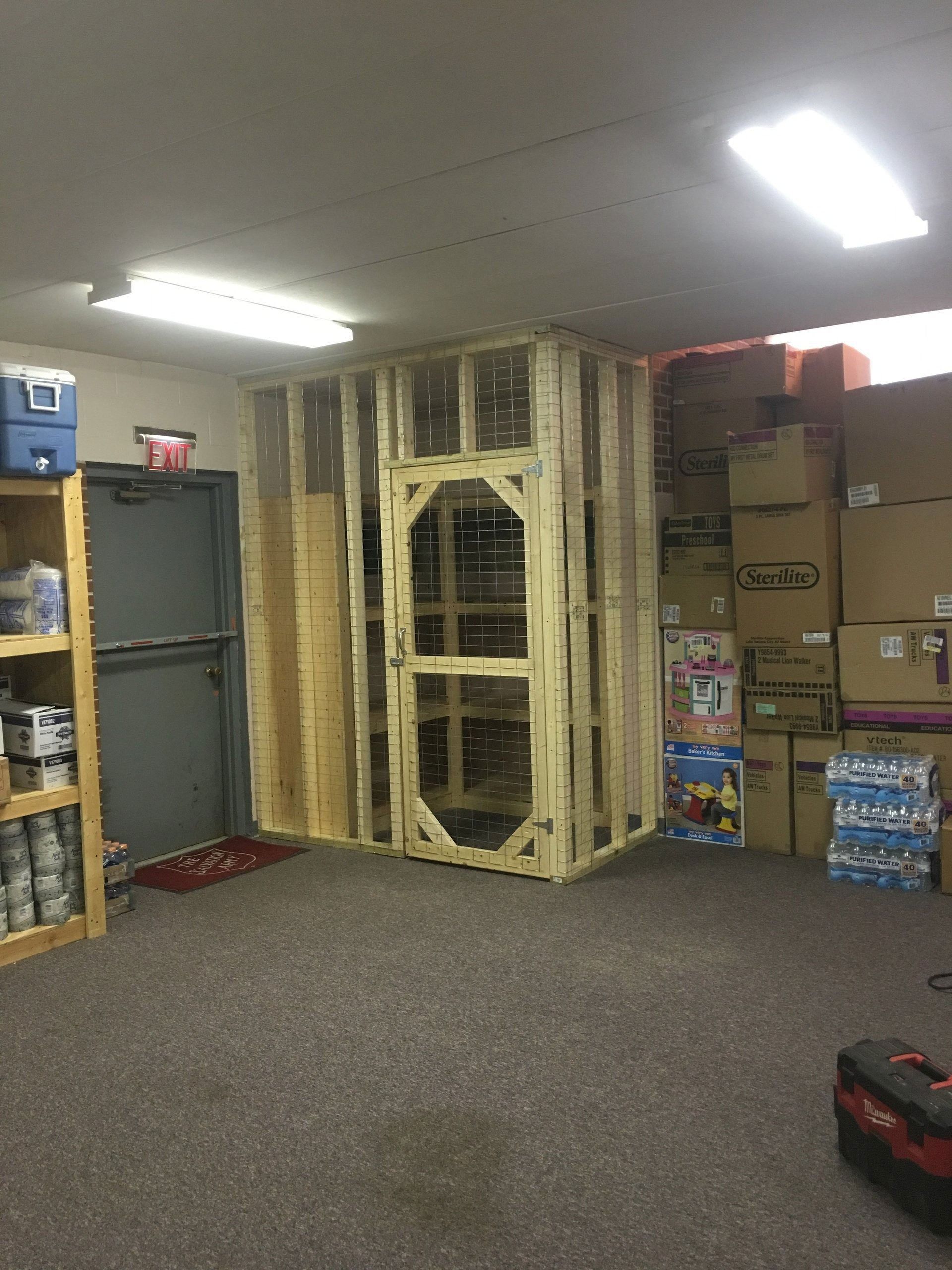 Basement storage room with stacked boxes, a metal door, and a tall wooden structure in the center.